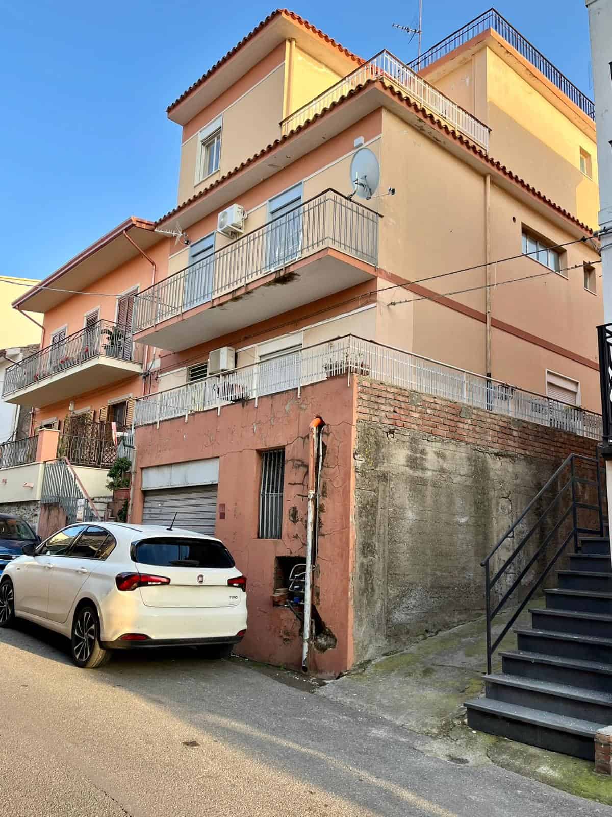 Appartamento residenziale su più livelli in edificio color pesca con balconi e terrazza, situato in zona urbana con auto parcheggiate e scale esterne, in un contesto di quartiere urbano.