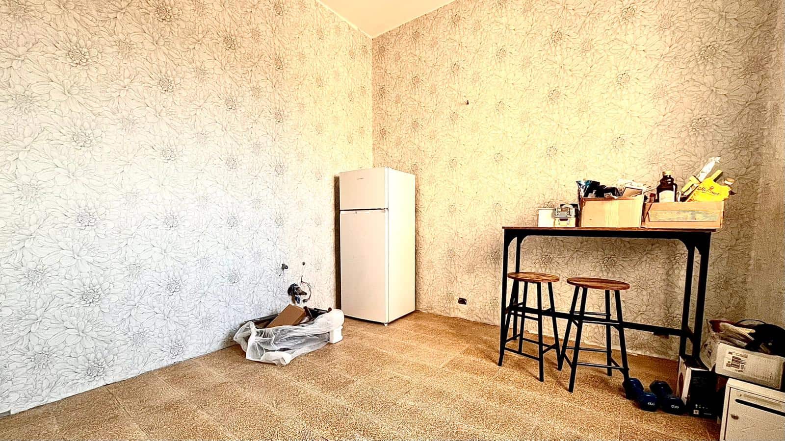 Lavatrice e frigorifero in una stanza vuota con pareti beige e pavimento in legno, spazio per ristrutturazione o arredamento.