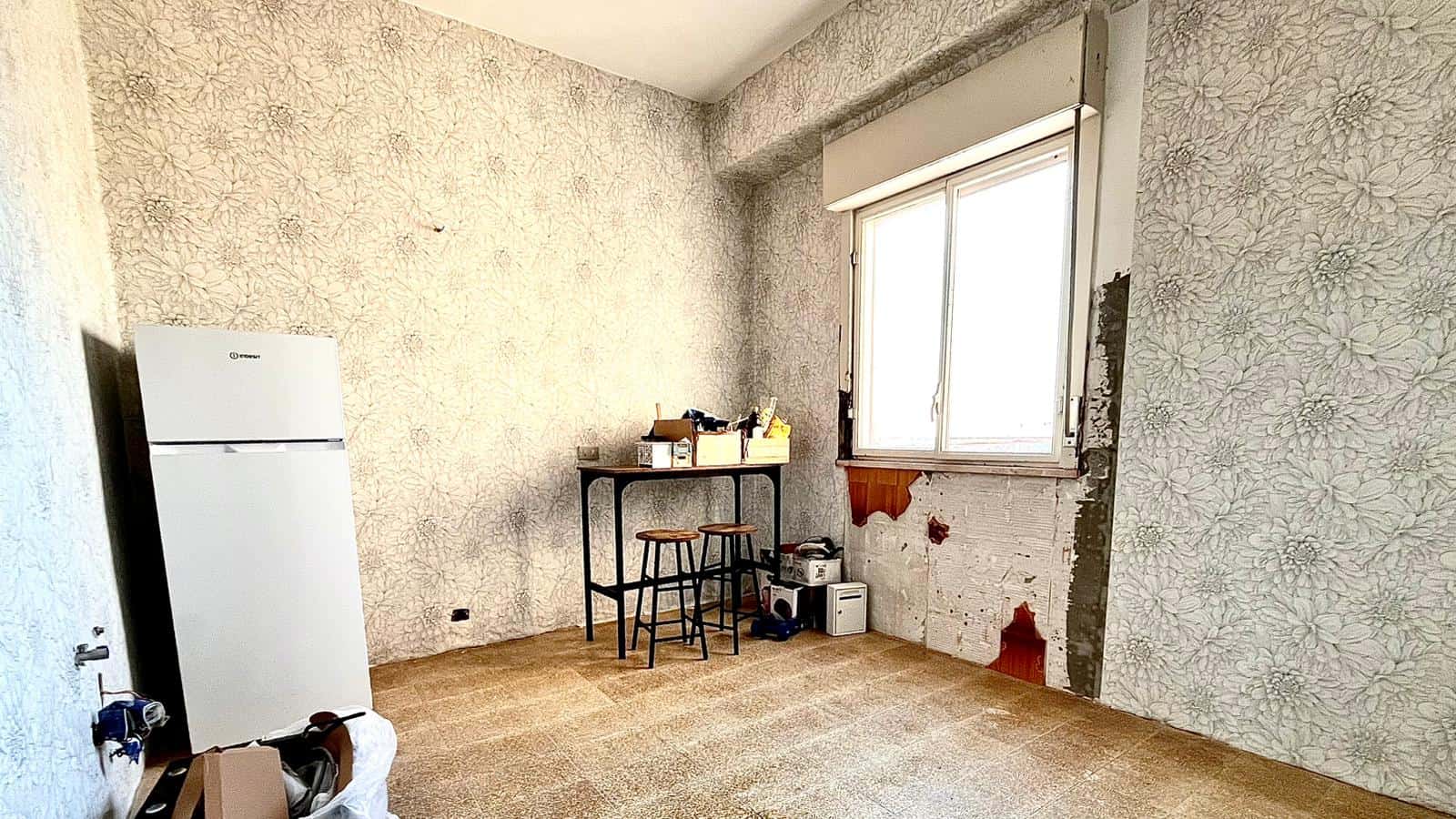 Spazio vuoto in una stanza da ristrutturare con pareti in fase di rivestimento, finestra grande e mobili minimalisti, ideale per rinnovare e personalizzare l'ambiente abitativo.