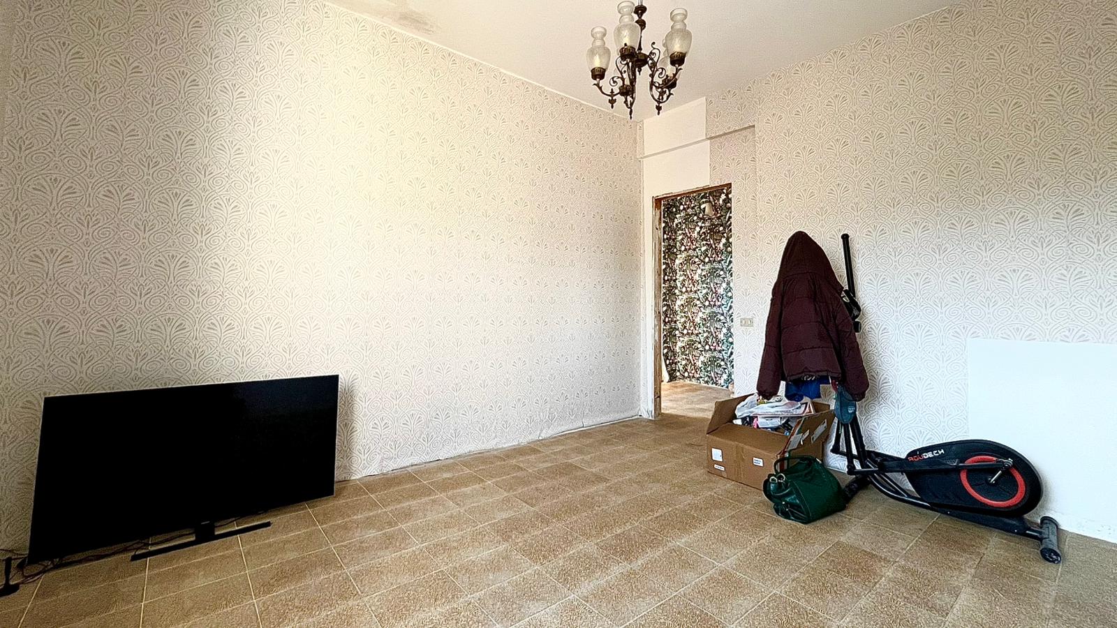 Ampia stanza vuota con pareti decorate, pavimento in piastrelle e lampadario centrale, pronta per essere arredata e personalizzata.