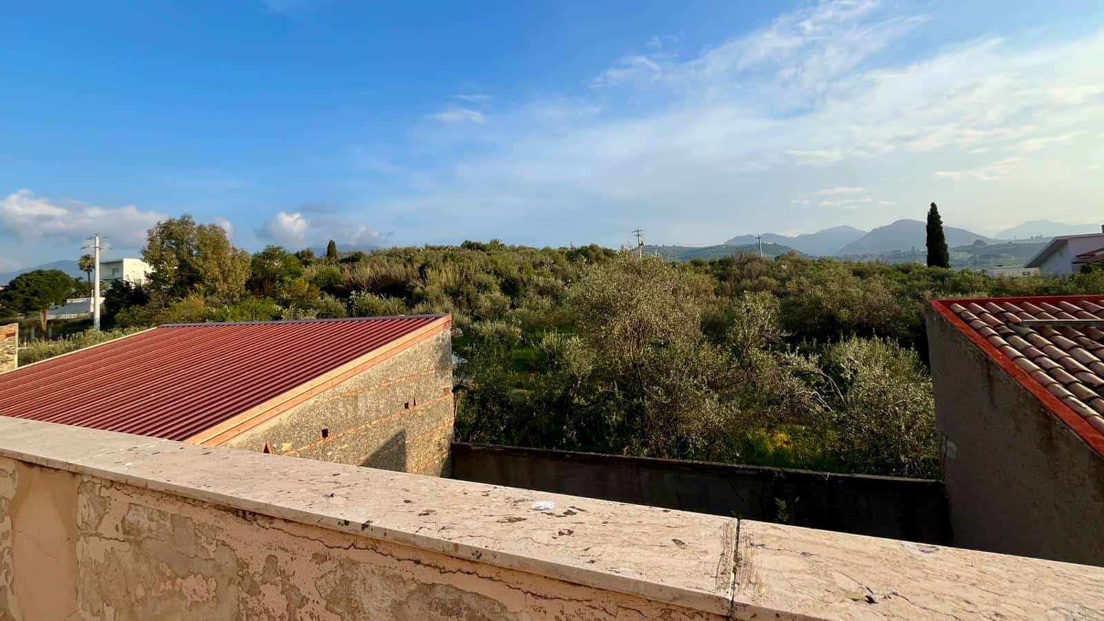 Vista panoramica di un paesaggio rurale con colline e vegetazione verde, cielo sereno e nuvole leggere, vista da una terrazza o balcone di una proprietà immobiliare in Italia.