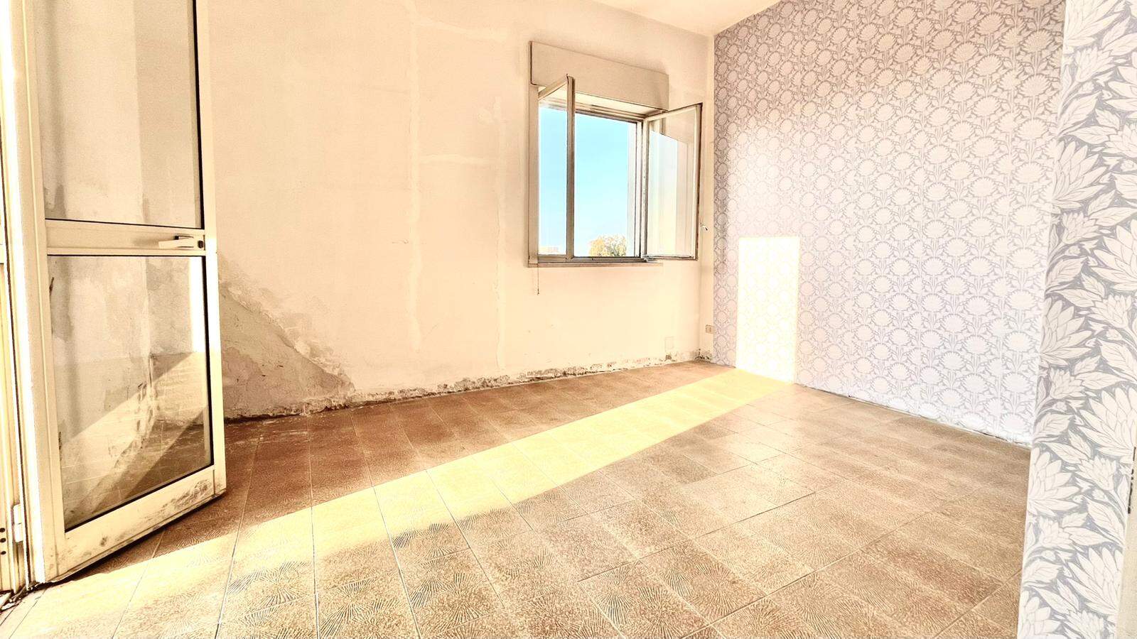 Ampio soggiorno vuoto con pareti chiare, pavimento in piastrelle e finestra aperta che lascia entrare luce naturale, pronto per arredamento e personalizzazione.