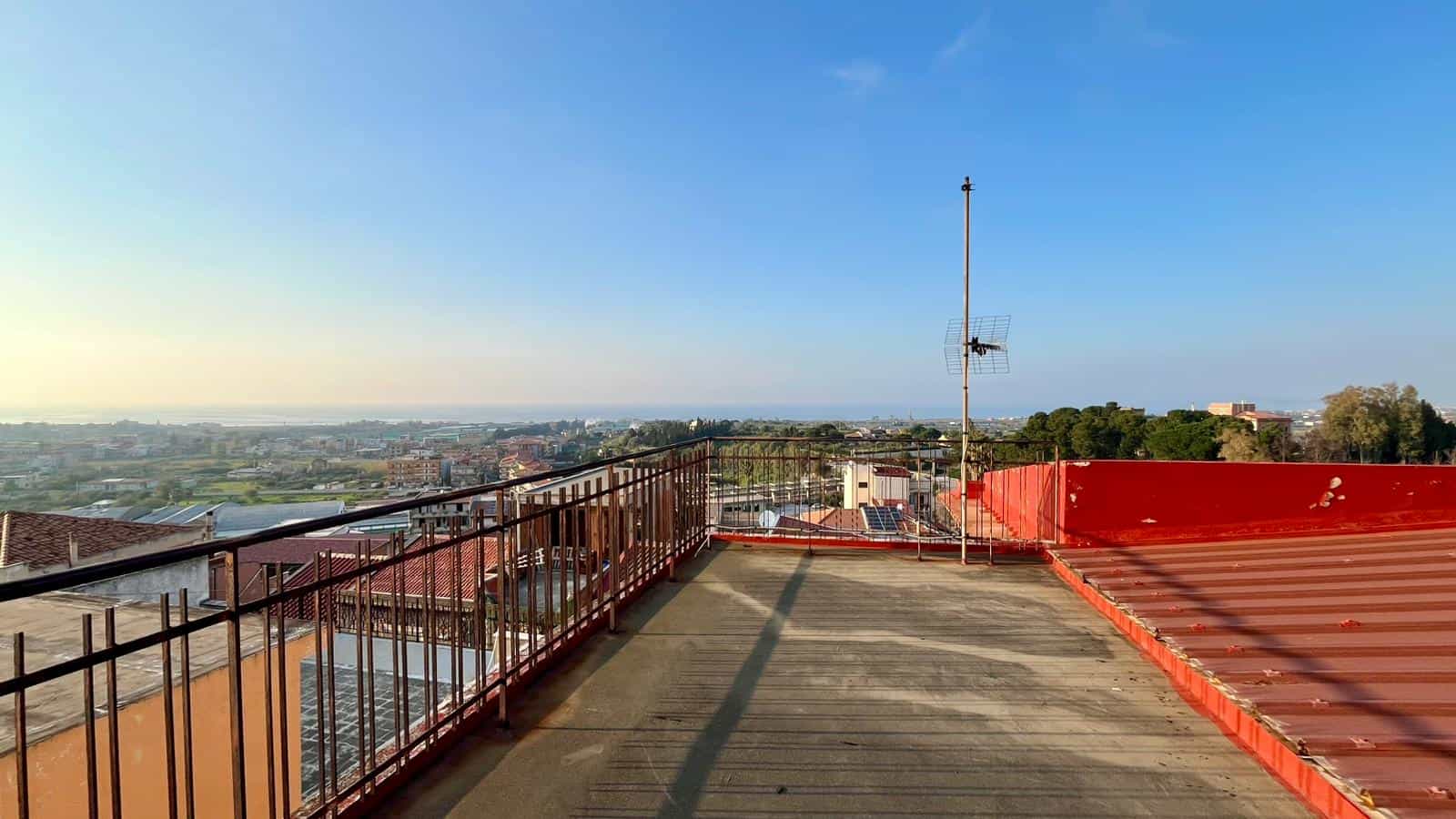 Vista panoramica dal tetto di un edificio con ringhiera in metallo, antenna e vista sulla città al tramonto, ideale per immobili residenziali e commerciali a NextCasa.