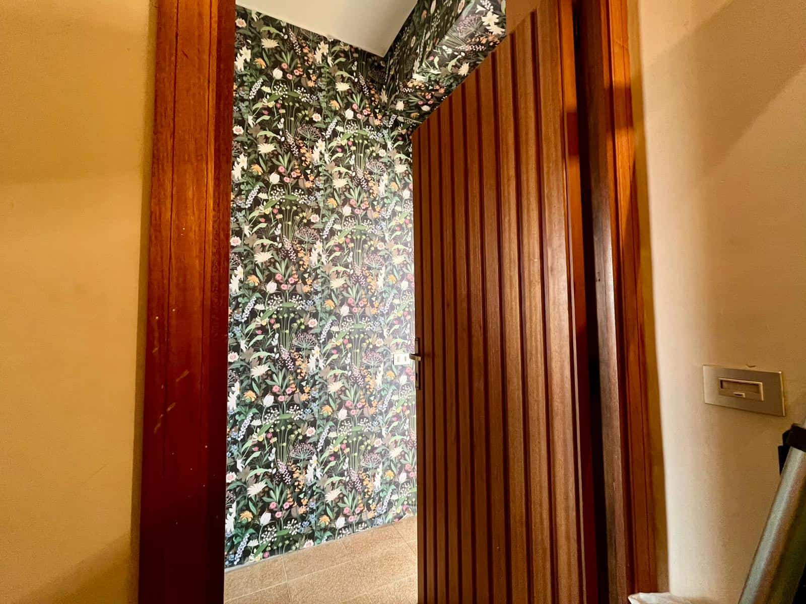 Ampia porta scorrevole in legno che separa due ambienti con parete decorativa a motivi botanici colorati, in un interno moderno e accogliente.