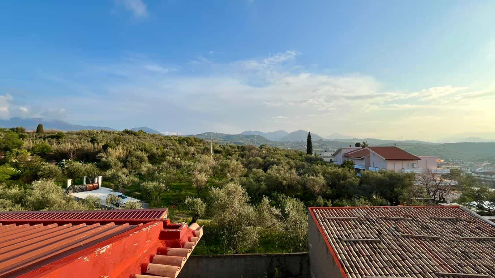 VISTA PANORAMICA di un paesaggio collinare con case e vegetazione, cielo sereno e montagne sullo sfondo, ideale per immobili e terreni in vendita o affitto a NextCasa.