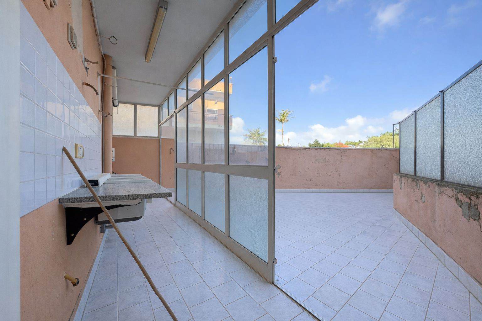 Balcone spazioso con pareti in vetro e vista panoramica, ideale per relax e momenti di convivialità all'aperto. Spazio luminoso e arioso, perfetto per arredare con piante e mobili da esterno.