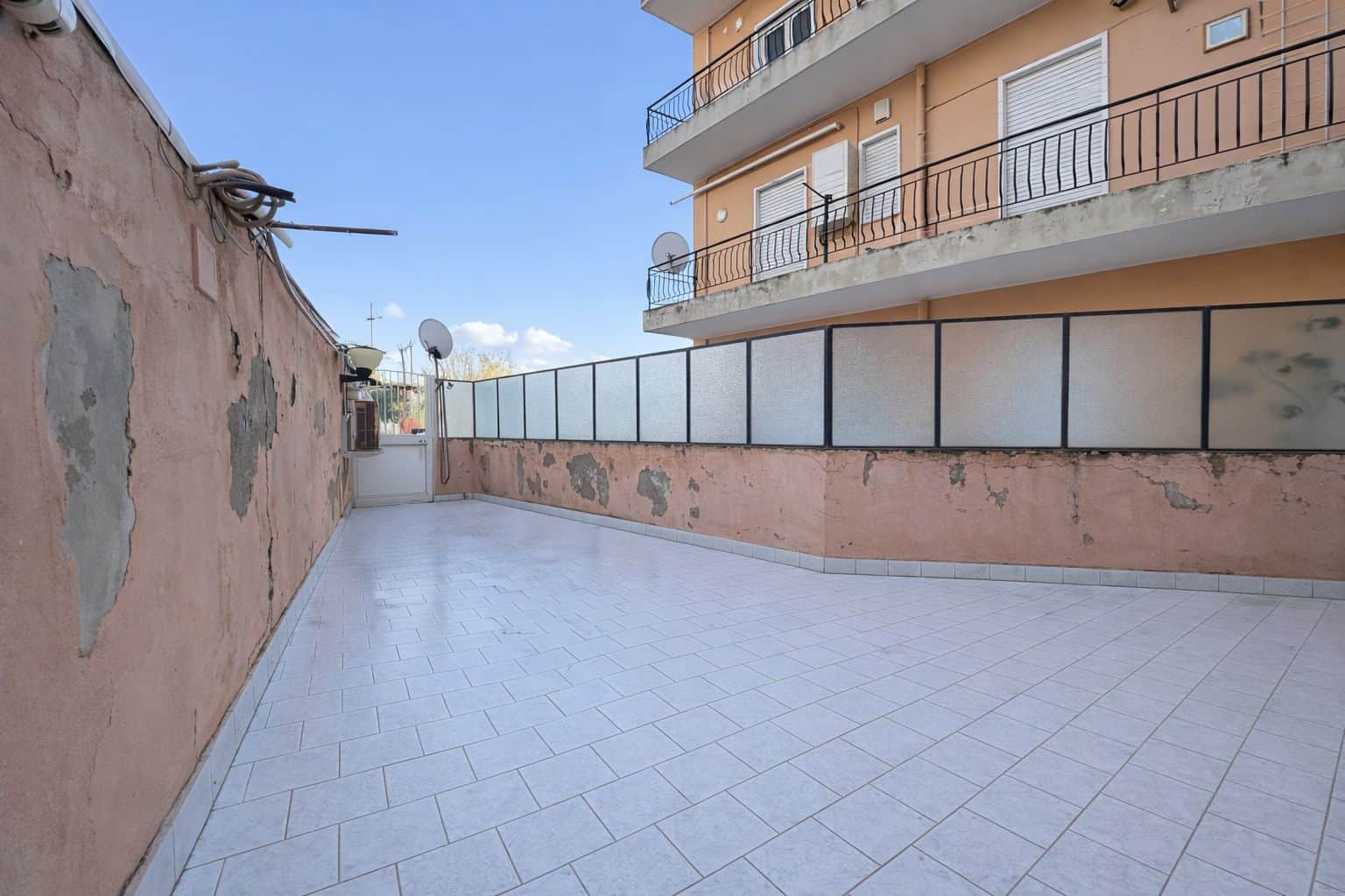 Ampio terrazzo esterno con vista su edificio residenziale, pavimentato in piastrelle chiare, ideale per relax e socializzazione, situato in zona urbana tranquilla e ben servita.