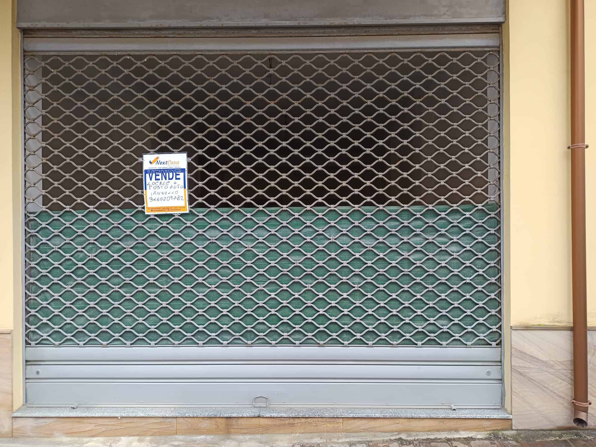 VENDESI negozio con serranda chiusa e insegna, posizione centrale in zona commerciale, ideale per attività o investimento immobiliare, con potenziale di riqualificazione e personalizzazione.