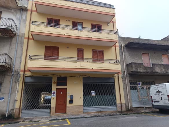 Porte blindate e balconi in ferro su edificio residenziale a Napoli, Italia, con facciata gialla e dettagli in legno, in zona urbana con negozi e servizi nelle vicinanze.