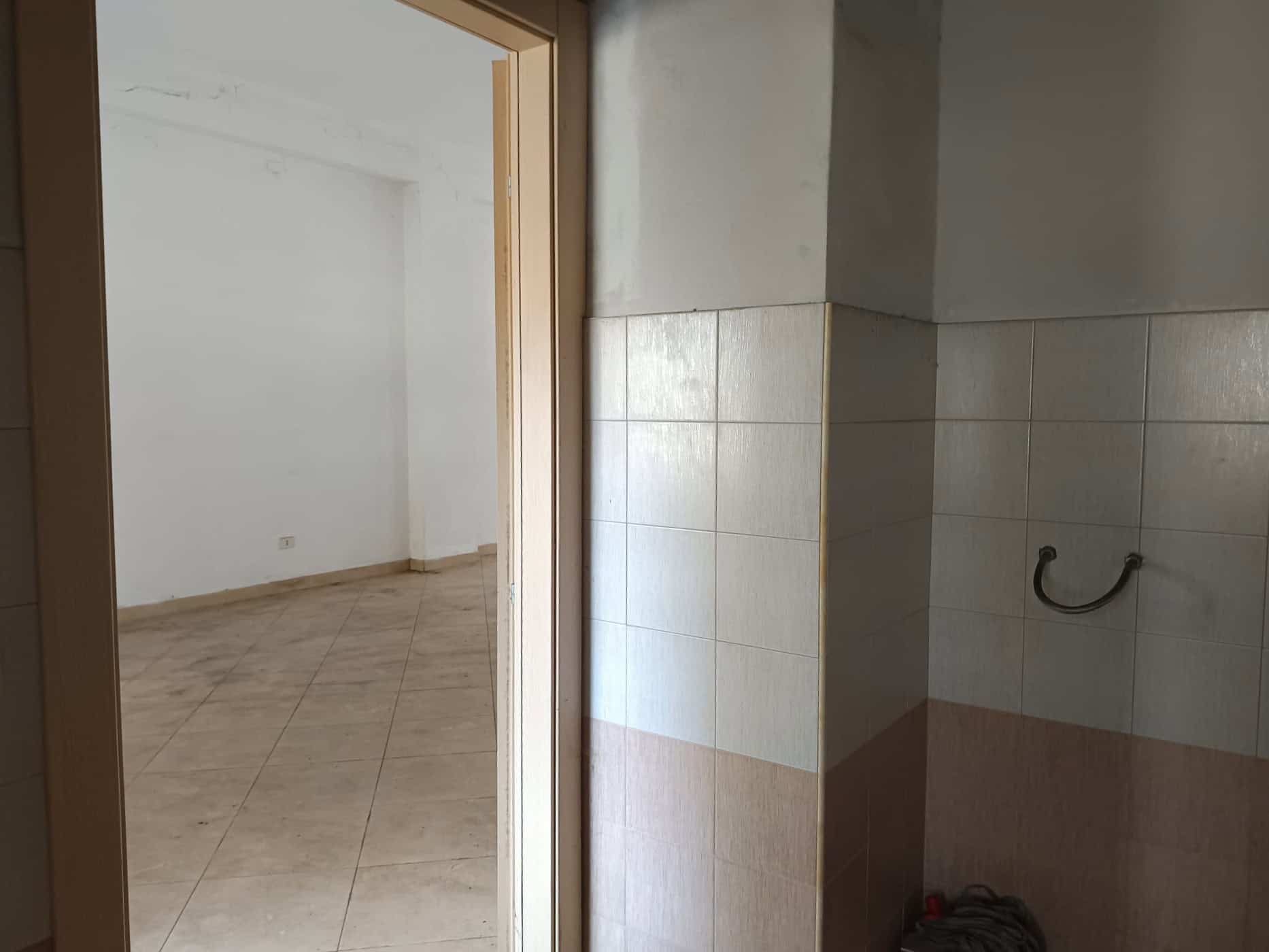 Un bagno in fase di ristrutturazione con pareti rivestite in piastrelle beige e un'area vuota pronta per installare sanitari, illuminato dalla luce naturale proveniente da una stanza adiacente.