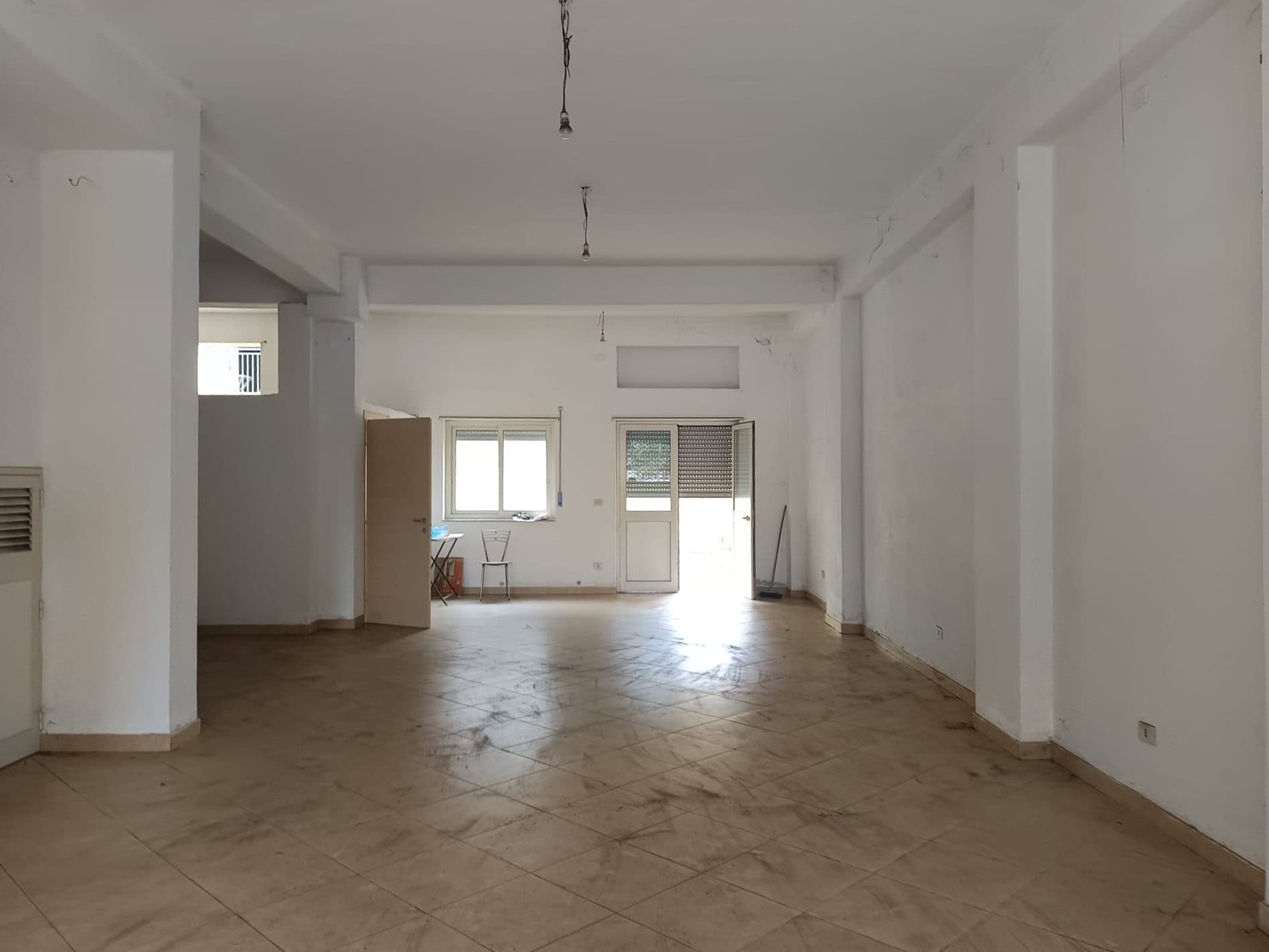 Ampia stanza vuota in un appartamento in fase di ristrutturazione, con pareti bianche e pavimento in piastrelle beige, pronta per essere personalizzata e arredato.