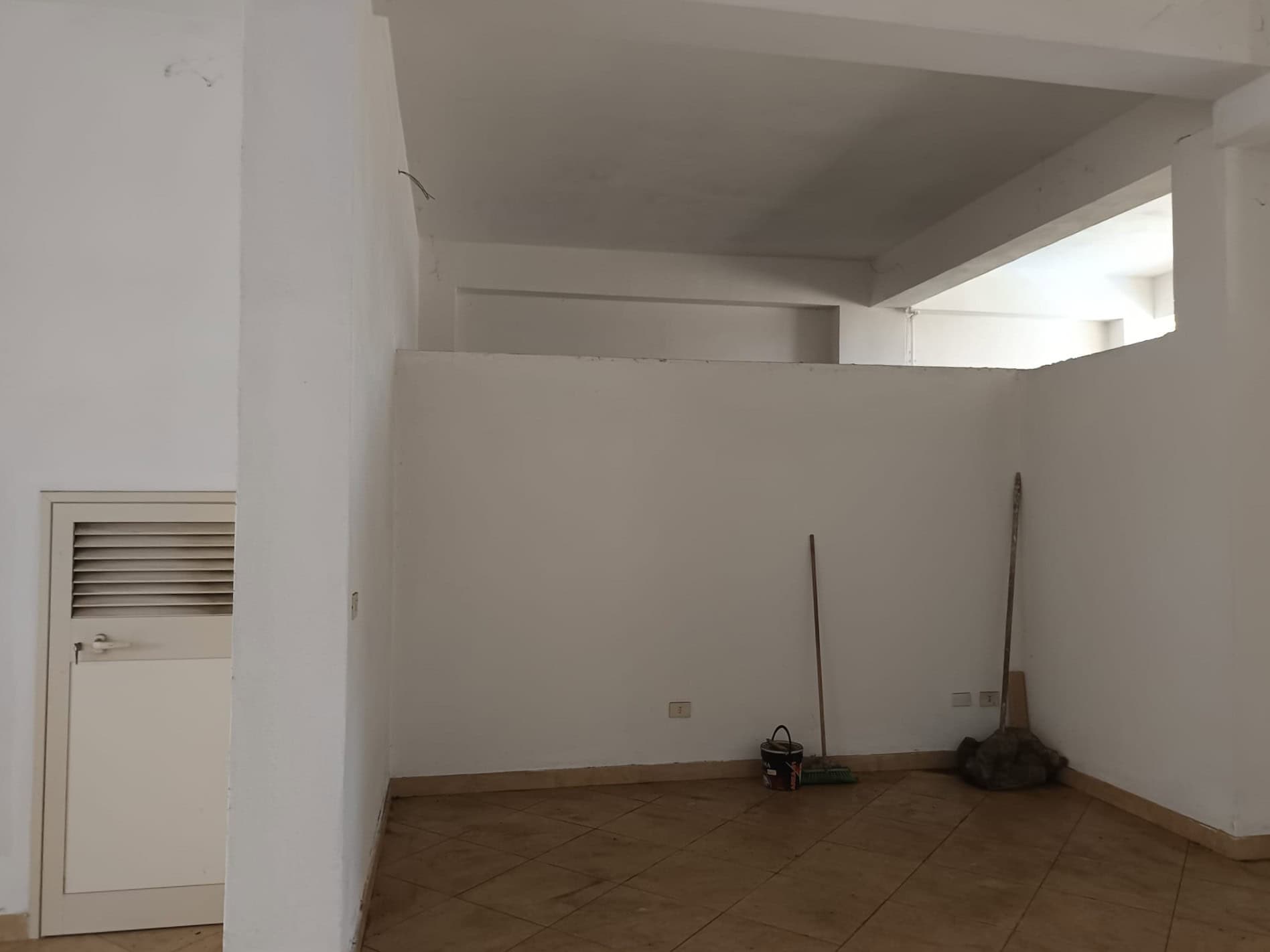 Spazio vuoto in un appartamento in fase di ristrutturazione con pareti bianche e pavimento in piastrelle beige, pronto per essere arredato e personalizzato.