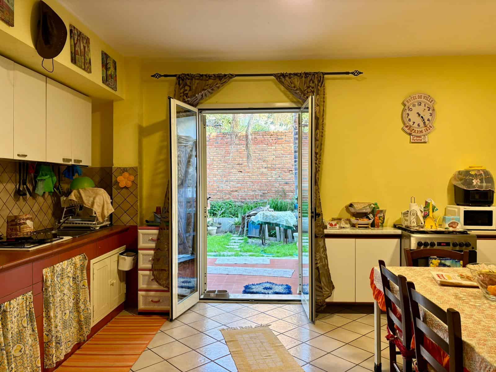 Aggiungi un'immagine di una cucina luminosa e accogliente con accesso al giardino, dotata di mobili moderni, elettrodomestici e decorazioni colorate, ideale per la vita familiare e il relax all'aperto.
