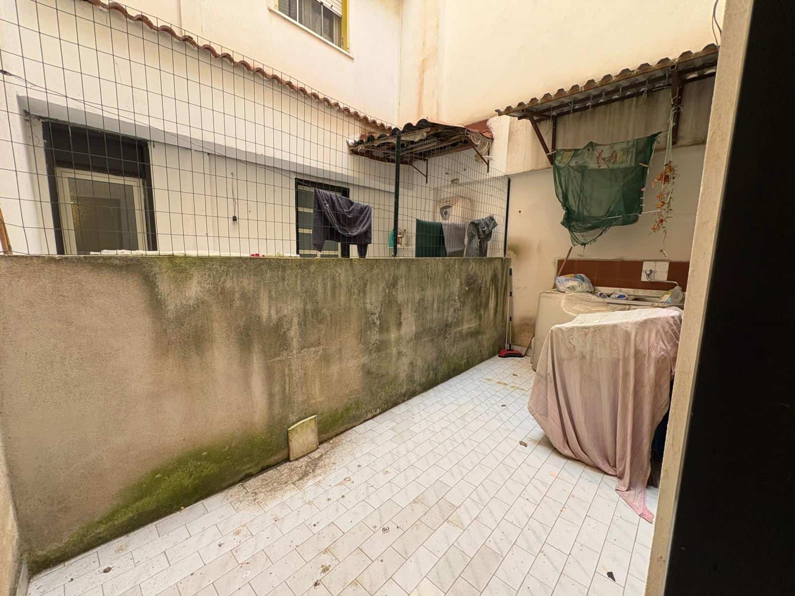 Lavanderia esterna con area di stenditura, pareti in cemento e pavimento in piastrelle, spazio funzionale per il bucato in un cortile di edificio residenziale.