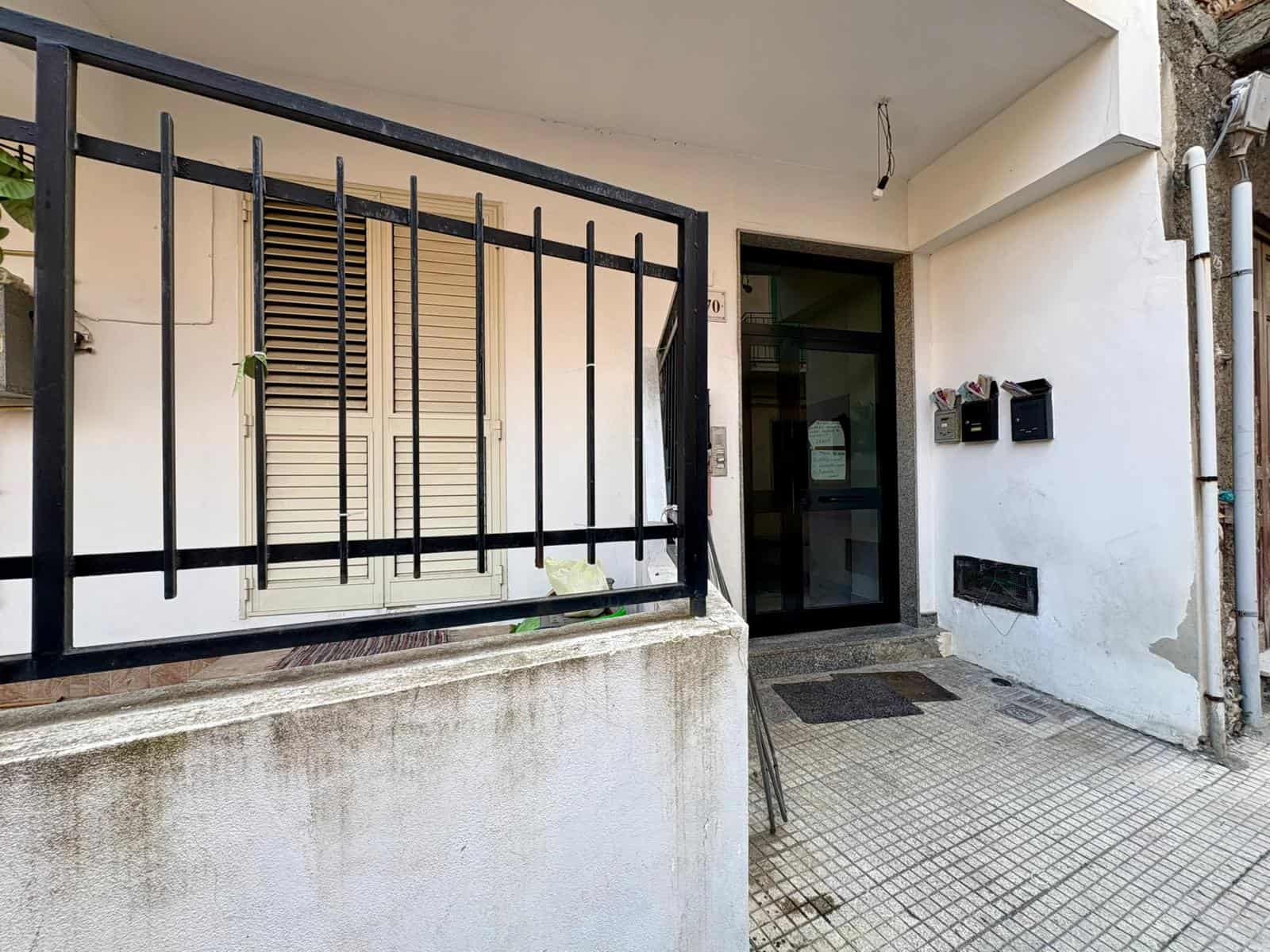 Cancello in ferro nero e ingresso condominiale in stile moderno, con pareti bianche e pavimentazione in piastrelle.