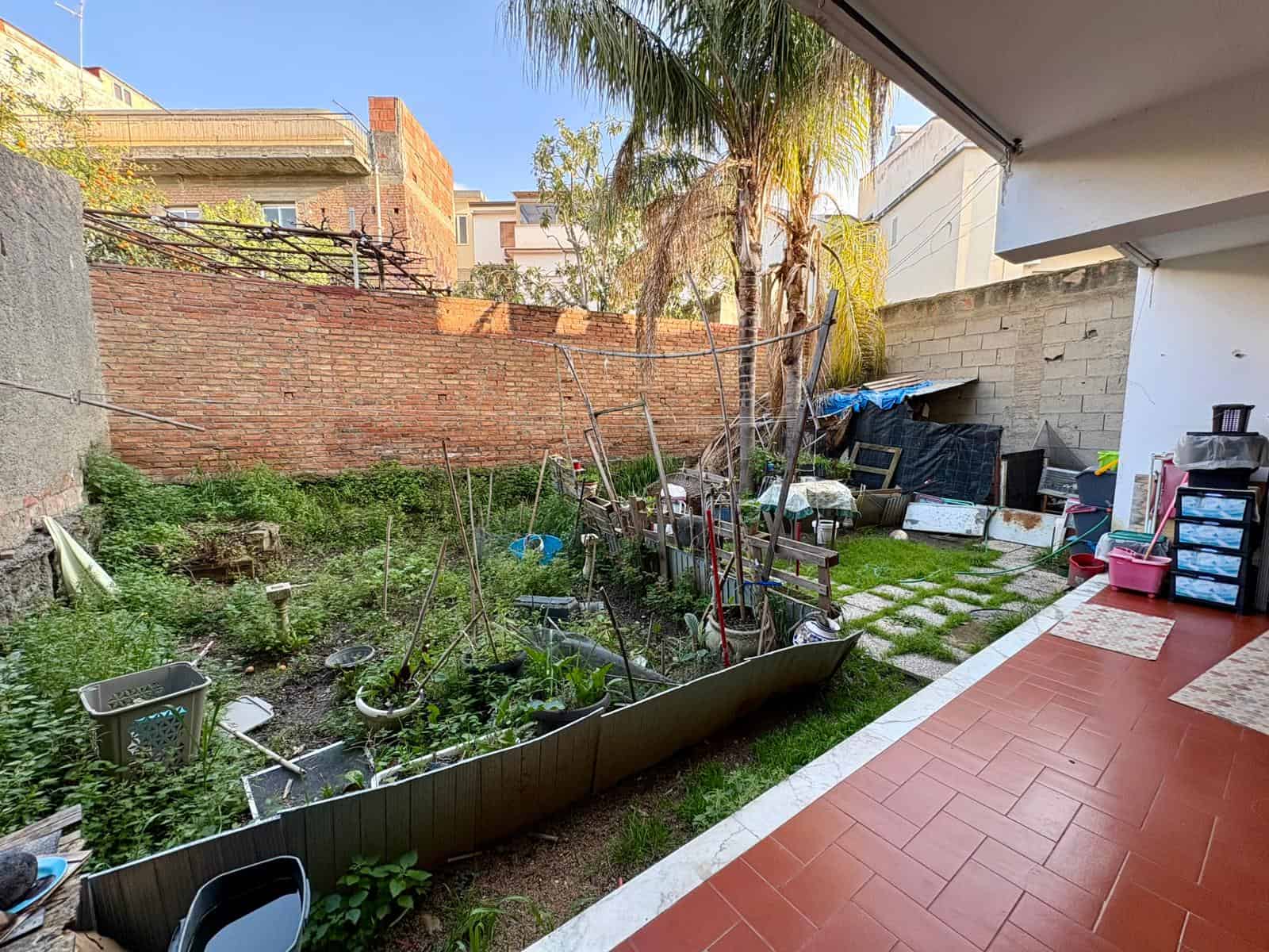 Piantagione urbana con piante e ortaggi in un giardino privato, con area coperta e spazio per coltivare verdure e fiori, ideale per orticoltura domestica e relax all'aperto.