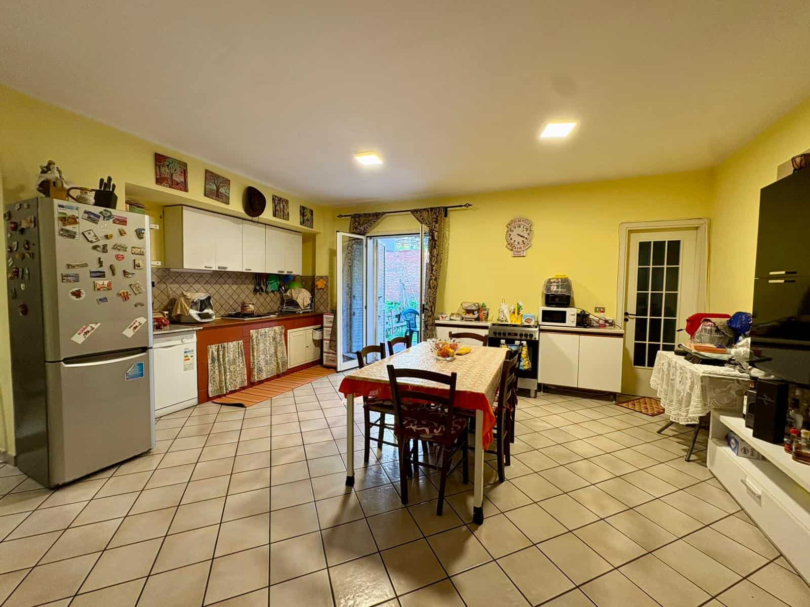 Cucina spaziosa e luminosa con mobili moderni, frigorifero, tavolo da pranzo e accessori, ambiente accogliente e funzionale.