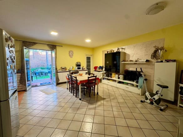 Ampia cucina soggiorno luminosa con tavolo da pranzo, accessori moderni, e porta finestra che conduce a un giardino esterno, ideale per vivere e intrattenere in casa.