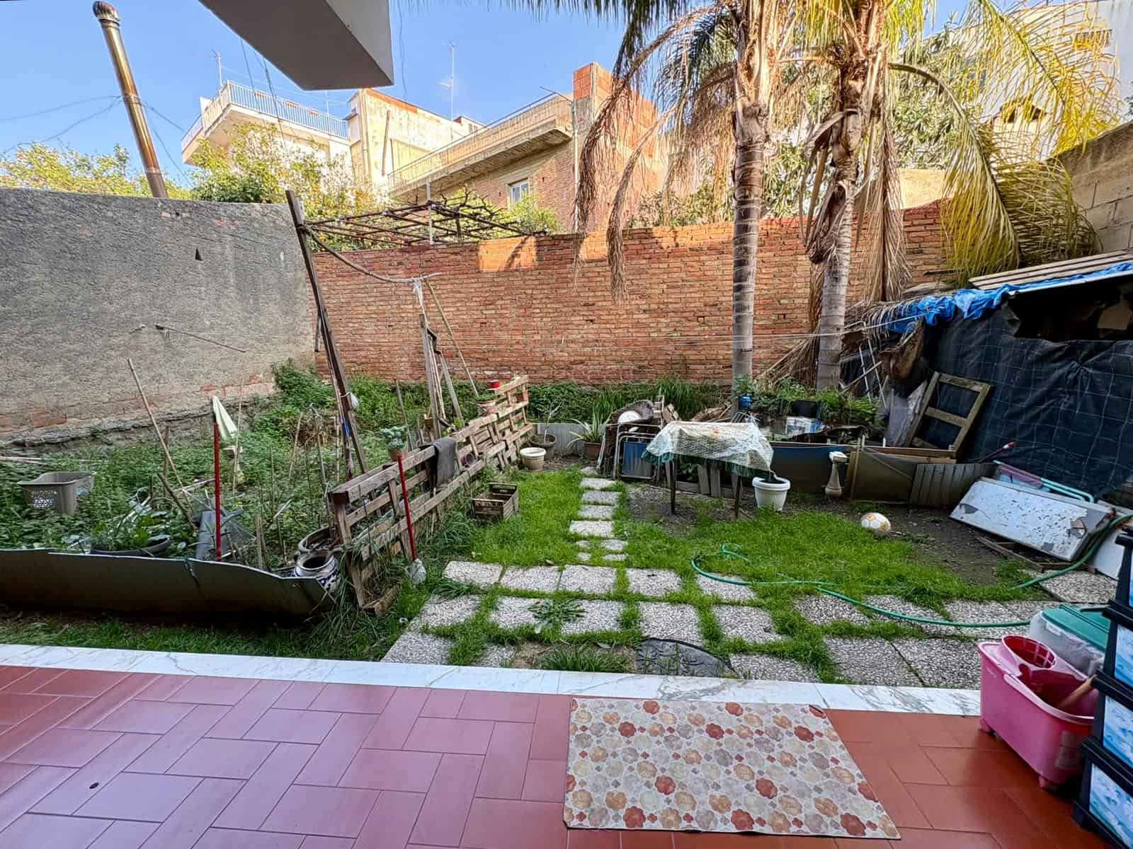 Pannello di giardino con piante, alberi di palma e area di relax con sedie e tavolo, spazio esterno ben curato e accogliente.