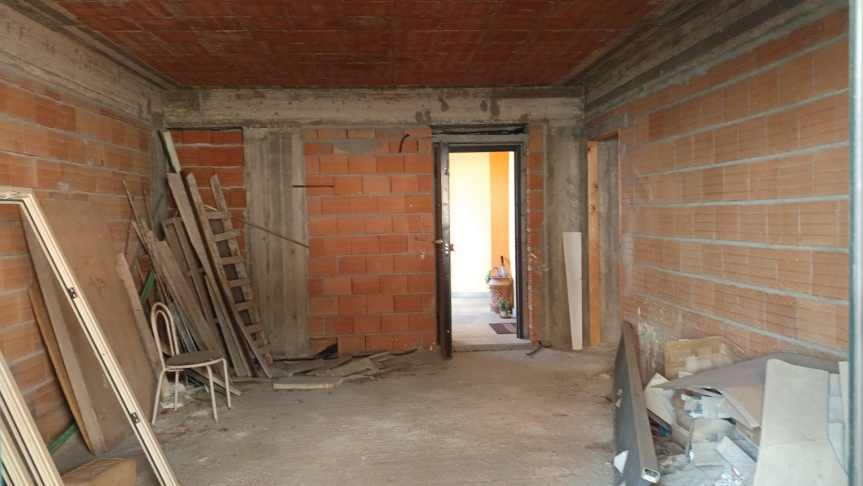 Immagine di un interno di un appartamento in fase di ristrutturazione con pareti in mattoni a vista e attrezzi da lavoro e materiali edili disposti all'interno.