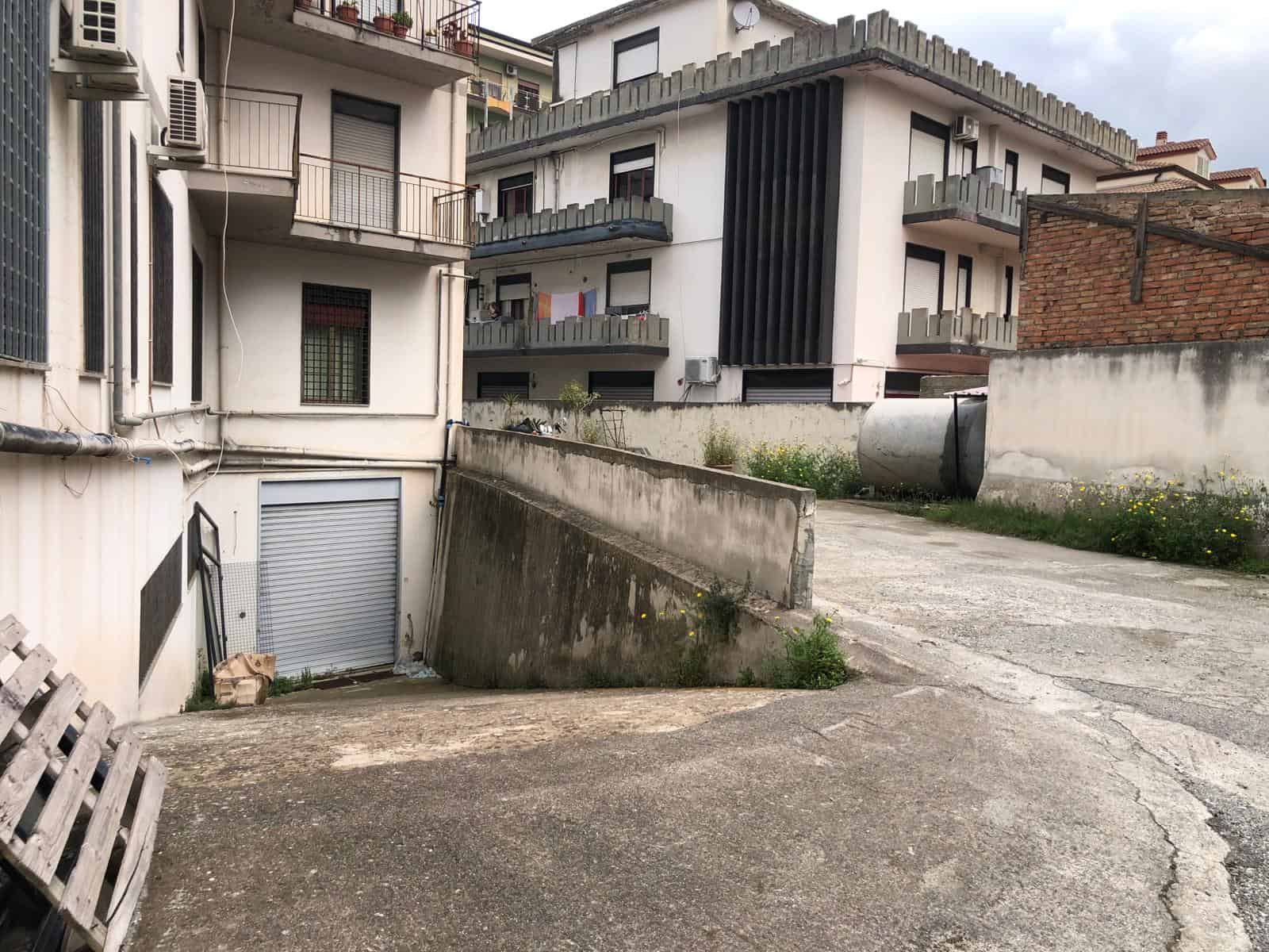 Un'area di parcheggio e accesso in pendenza tra edifici residenziali moderni e tradizionali in un quartiere urbano italiano.