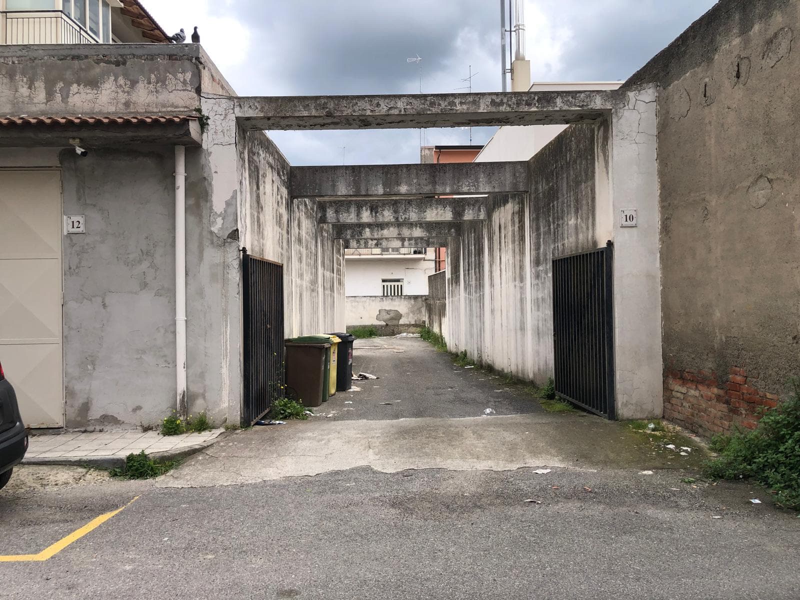 Cancello di ingresso in un cortile urbano con muri in cemento e cancelli in metallo, ambiente residenziale con spazi aperti e parcheggio.