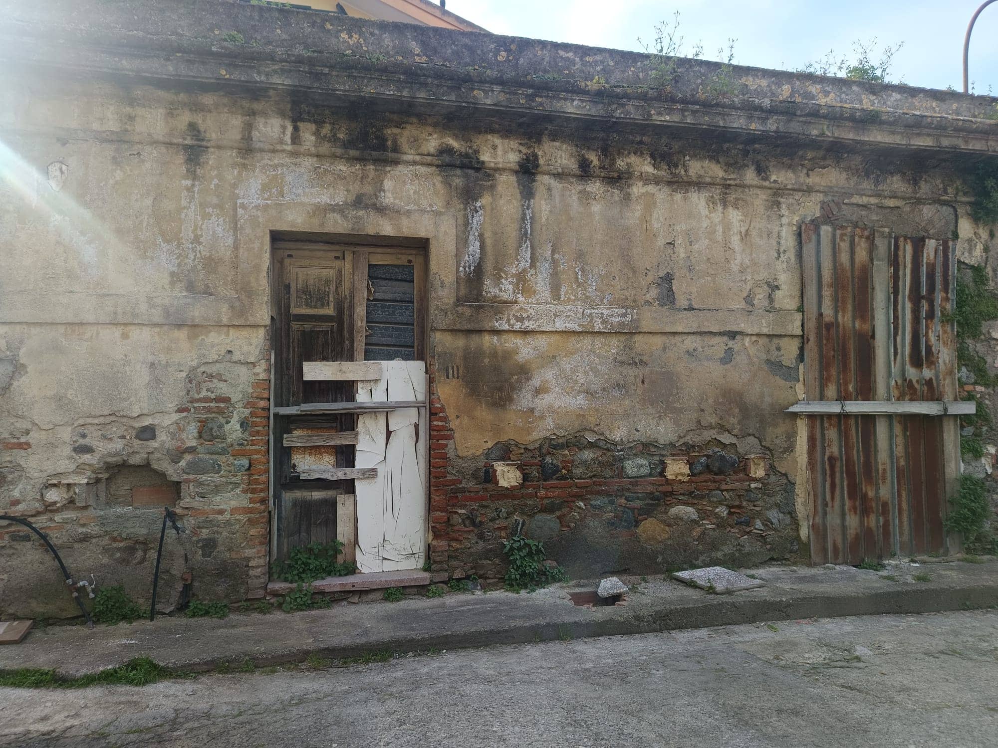 Vecchio muro in pietra e mattoni con porta in legno e recinzione in lamiera arrugginita, scenario urbano rustico e decadente, ideale per immagini di ristrutturazione o recupero edilizio.