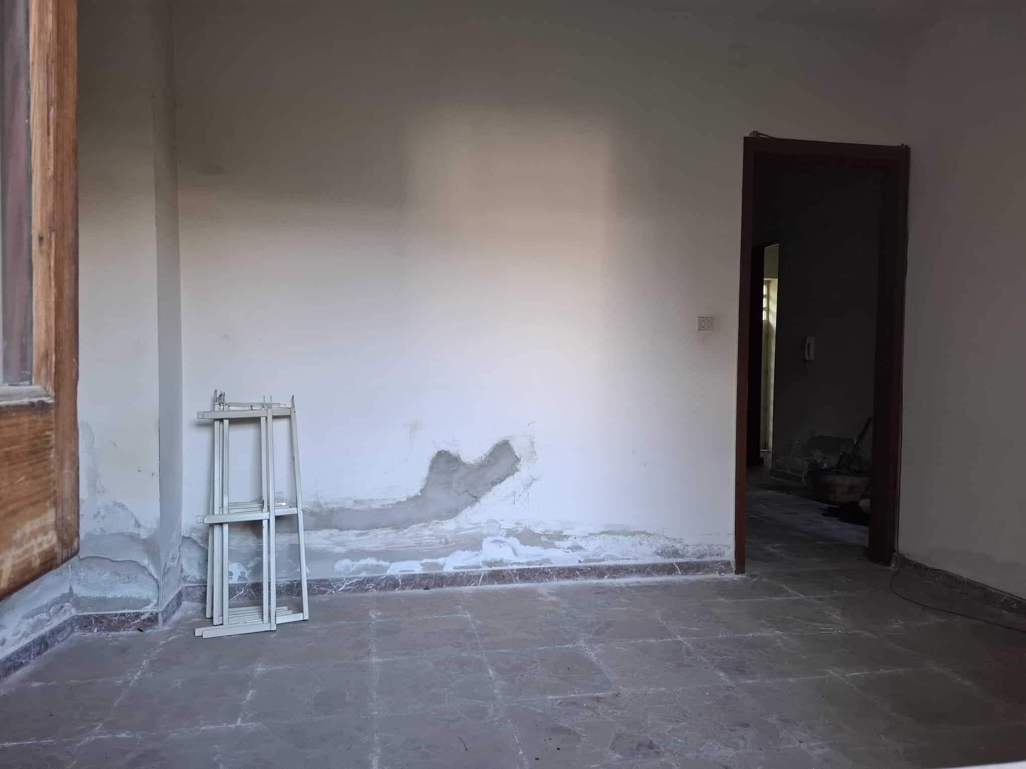Parete interna di una casa in fase di ristrutturazione con pareti bianche e pavimento in piastrelle, pronto per lavori di finitura e decorazione.