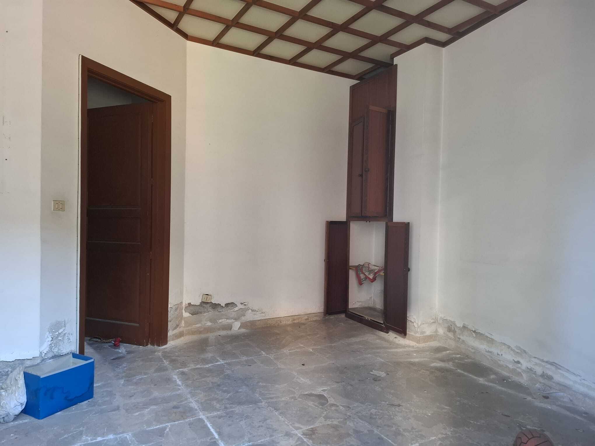Riparazione e ristrutturazione di un interno di casa, con pareti bianche, pavimento in pietra e armadio in legno, pronto per essere personalizzato o arredato.