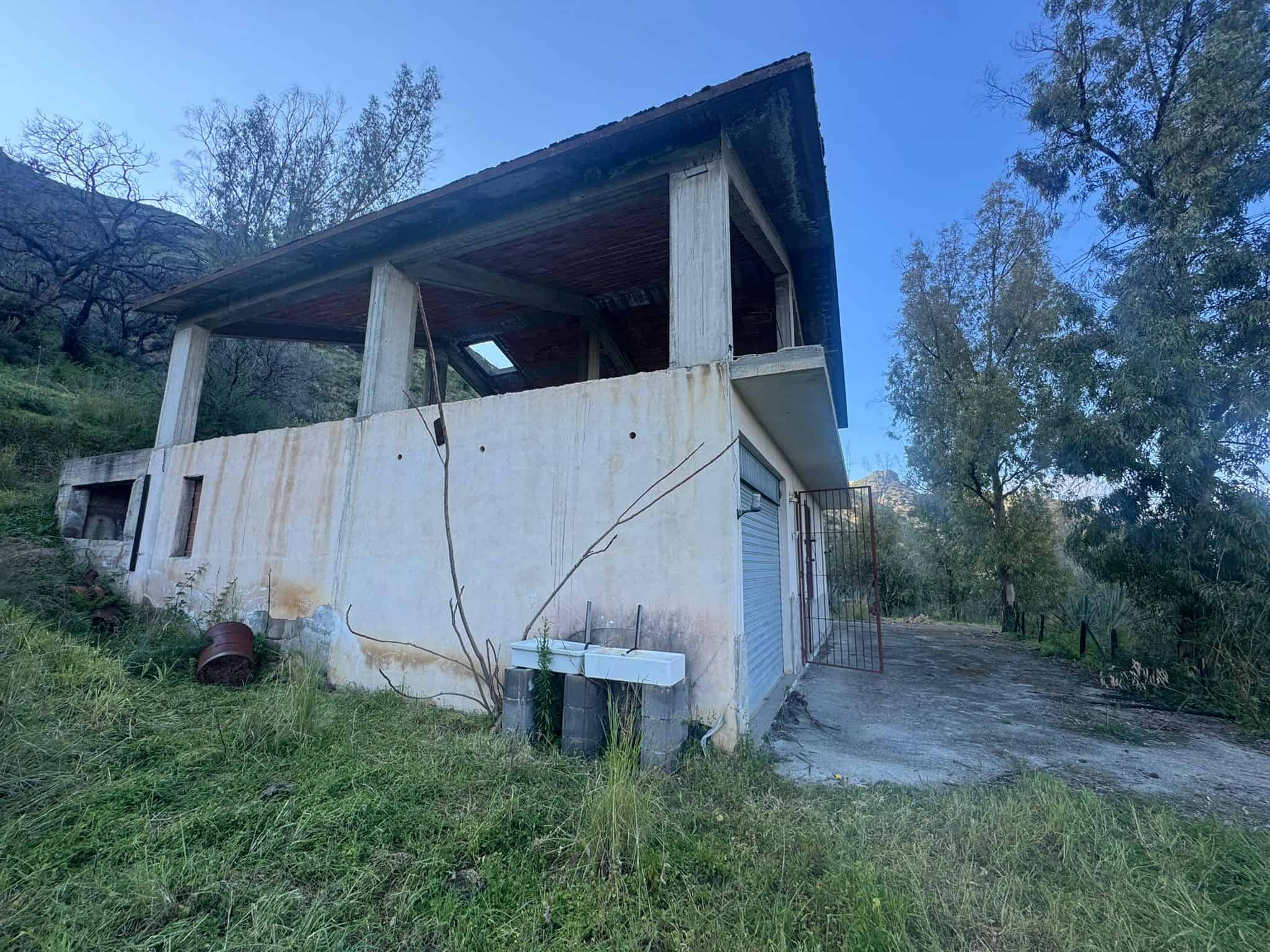 Abbandono di una casa rustica su una collina con vista sulla natura, struttura in cemento e legno, ideale per ristrutturazione o investimento immobiliare in zona tranquilla e verde.