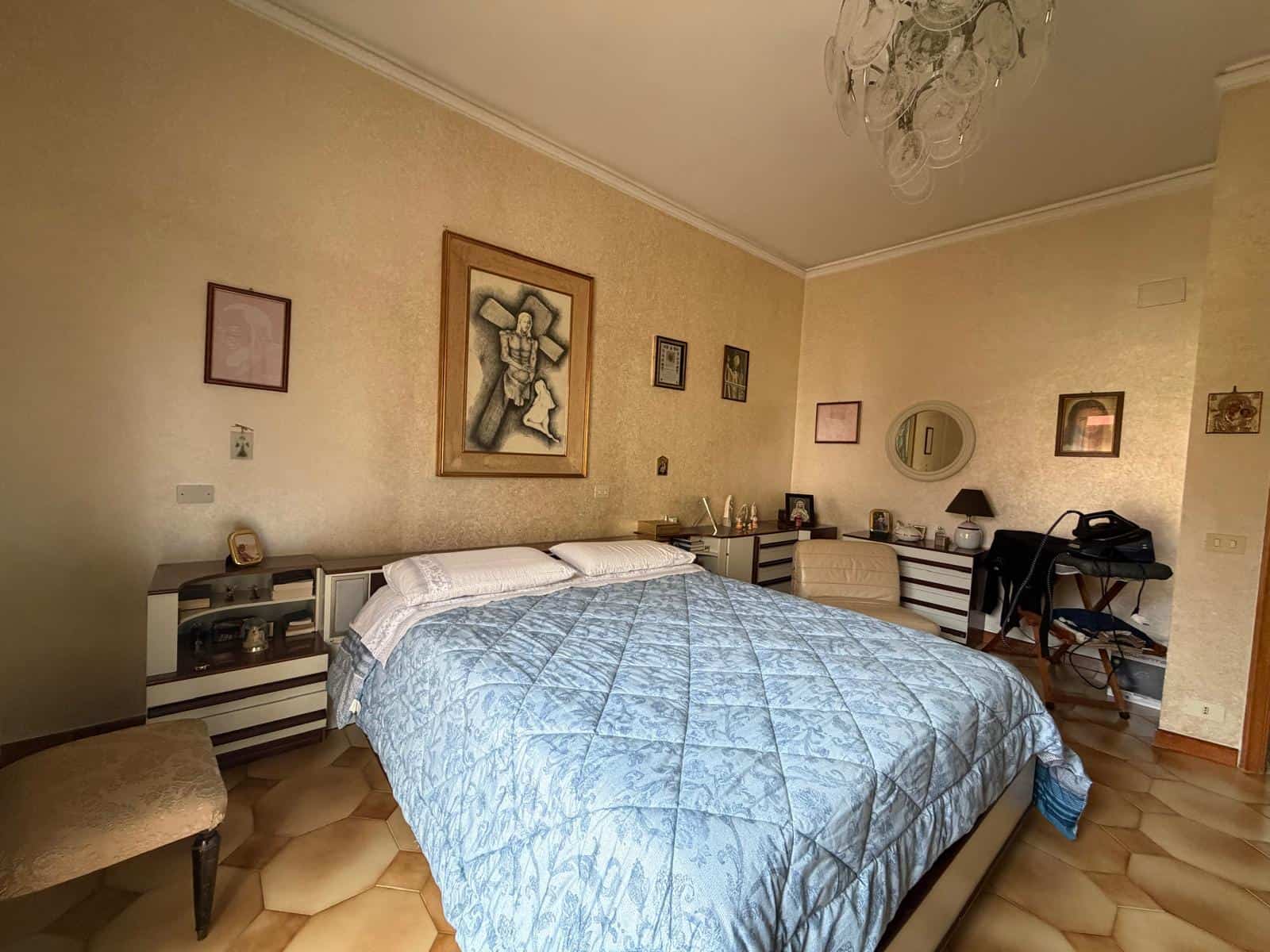 Riproduzione di una camera da letto spaziosa con pareti beige, arredi moderni e decorazioni artistiche, ideale per vivere in comfort e stile.