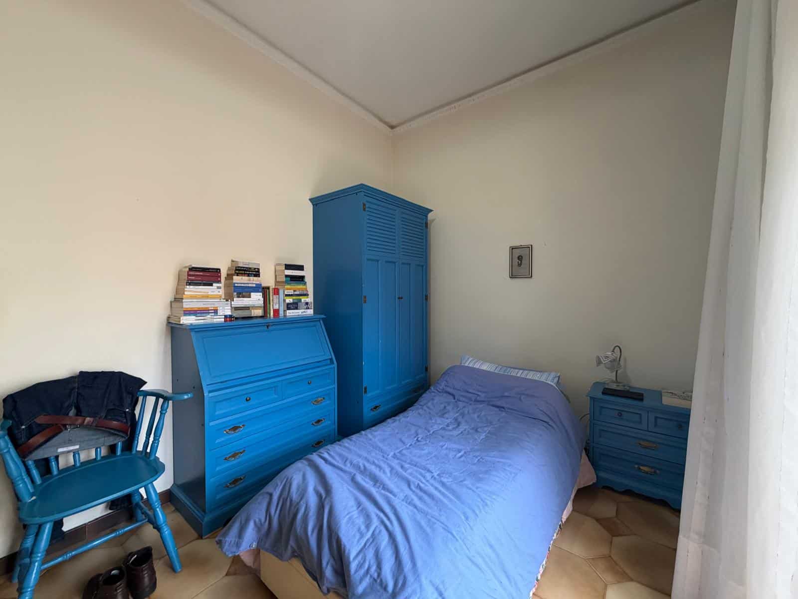 Riproduzione di una camera da letto con mobili blu, tra cui armadio, cassettiera e scrivania, con letto singolo e sedia, in un ambiente luminoso e semplice, ideale per ambienti moderni e minimalisti.