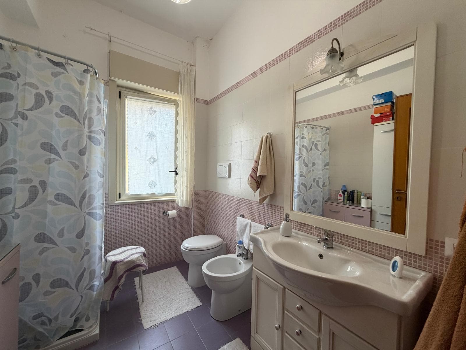 Lavabo e bagno con piastrelle bianche e rosa, specchio grande e armadietto, ambiente luminoso e funzionale, ideale per la casa o l'appartamento.