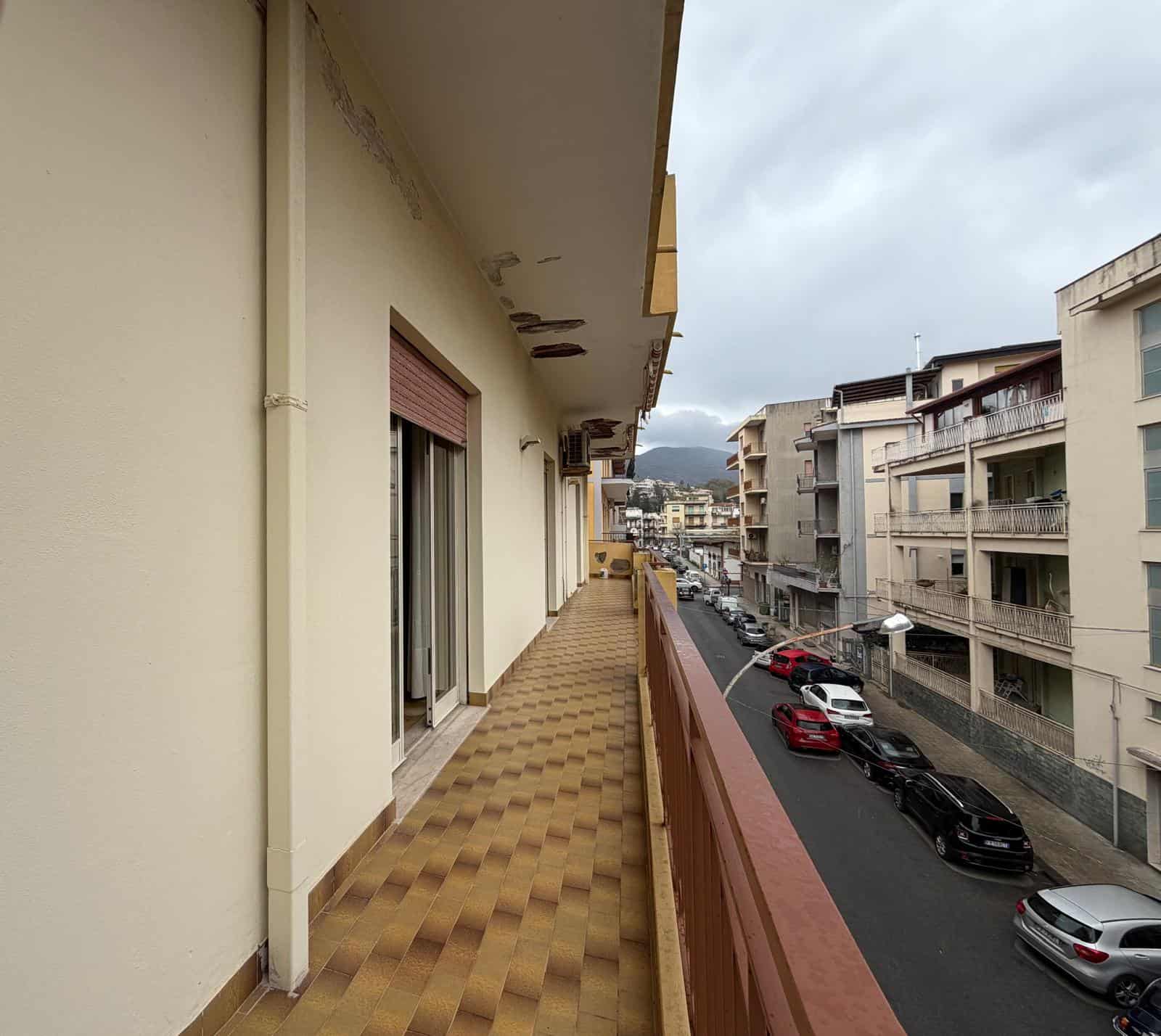 Balcone di un appartamento in un quartiere urbano con vista sulle strade e edifici circostanti, in una giornata nuvolosa.