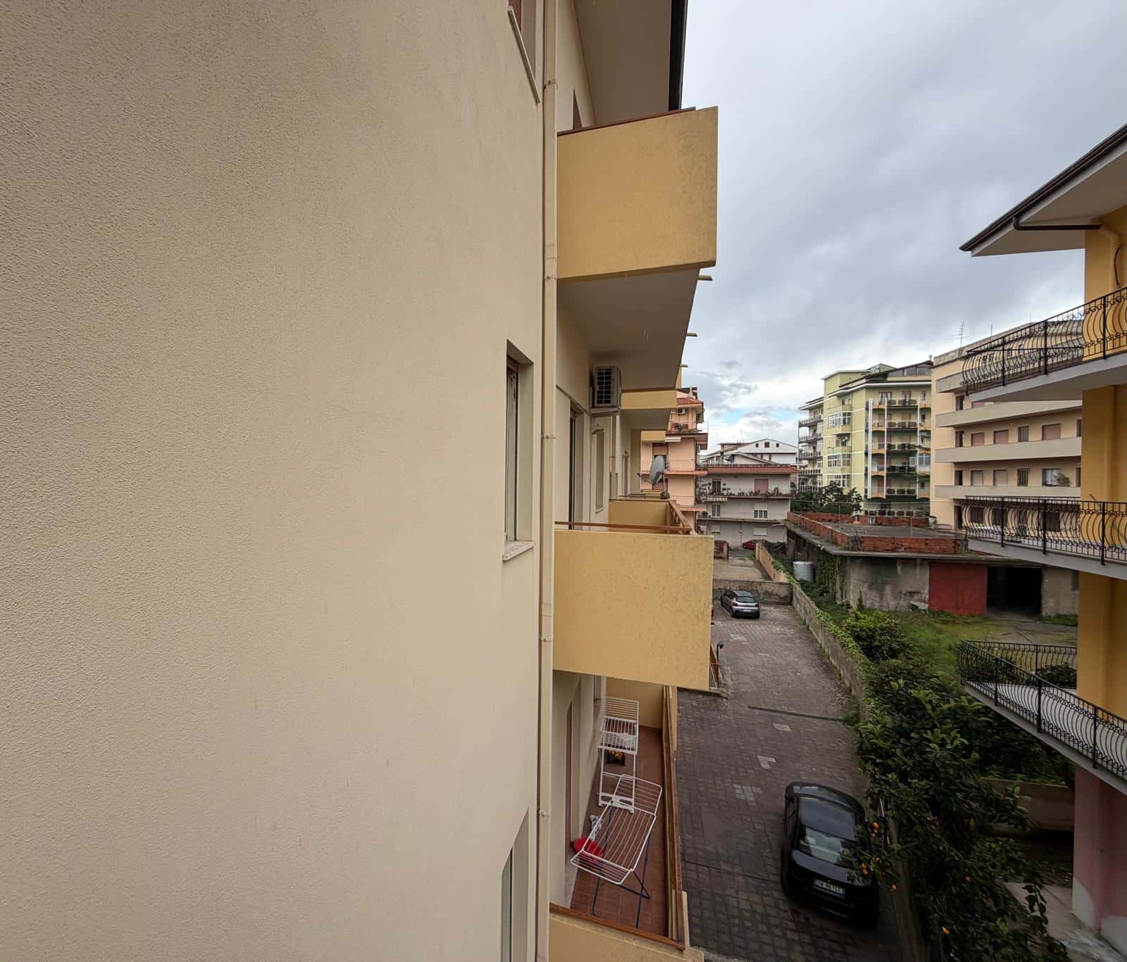 Vista di un cortile condominiale con parcheggio e balconi di appartamenti in un complesso residenziale urbano, cielo nuvoloso.