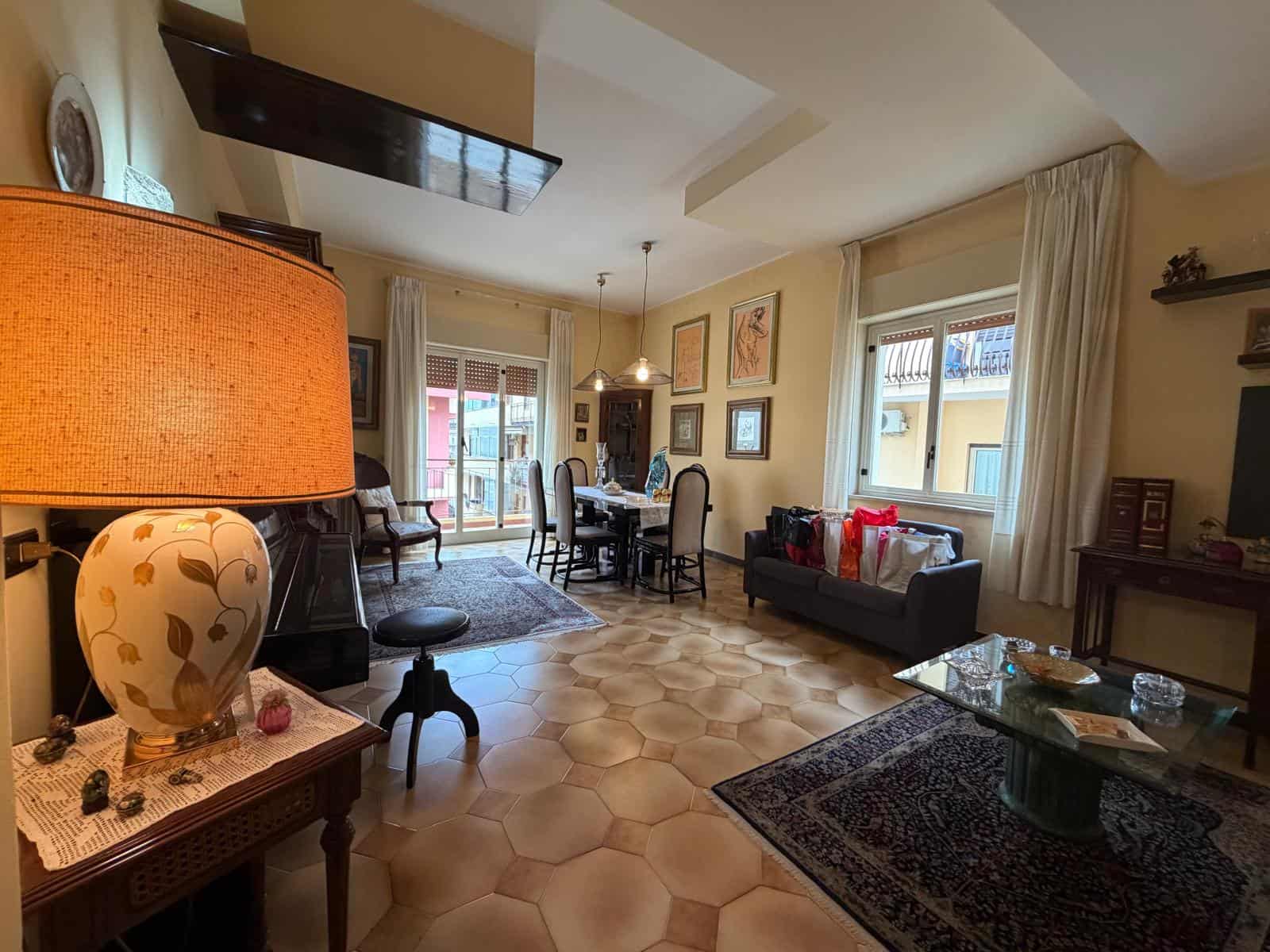 Interno di un soggiorno luminoso e accogliente con mobili eleganti, grandi finestre e decorazioni artistiche, ideale per vivere e ricevere ospiti.