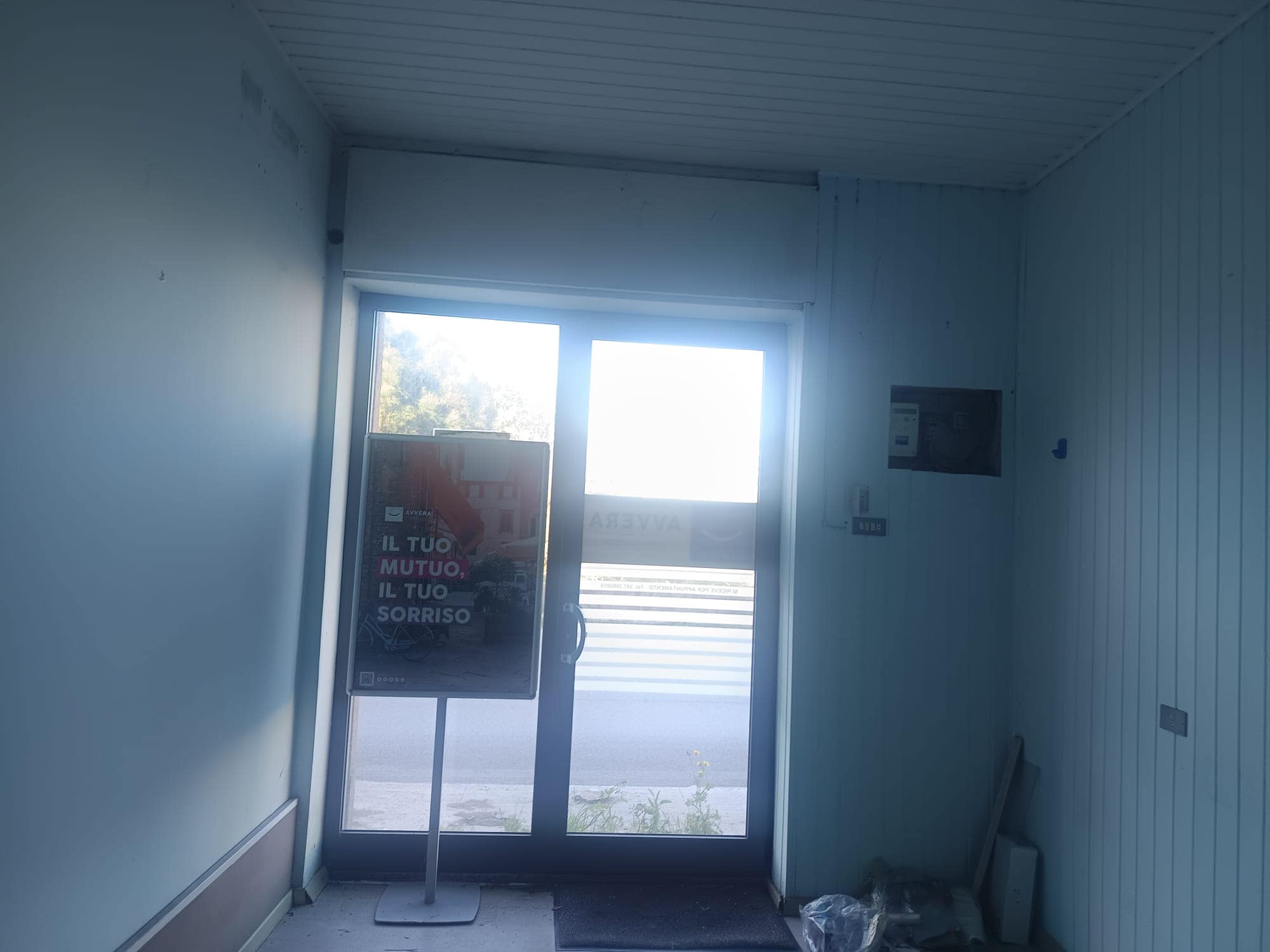 Cancello di ingresso con porta in vetro e finestra, ambiente interno luminoso e moderno, ideale per soluzioni abitative o commerciali, con vista sulla strada e spazio per arredi.