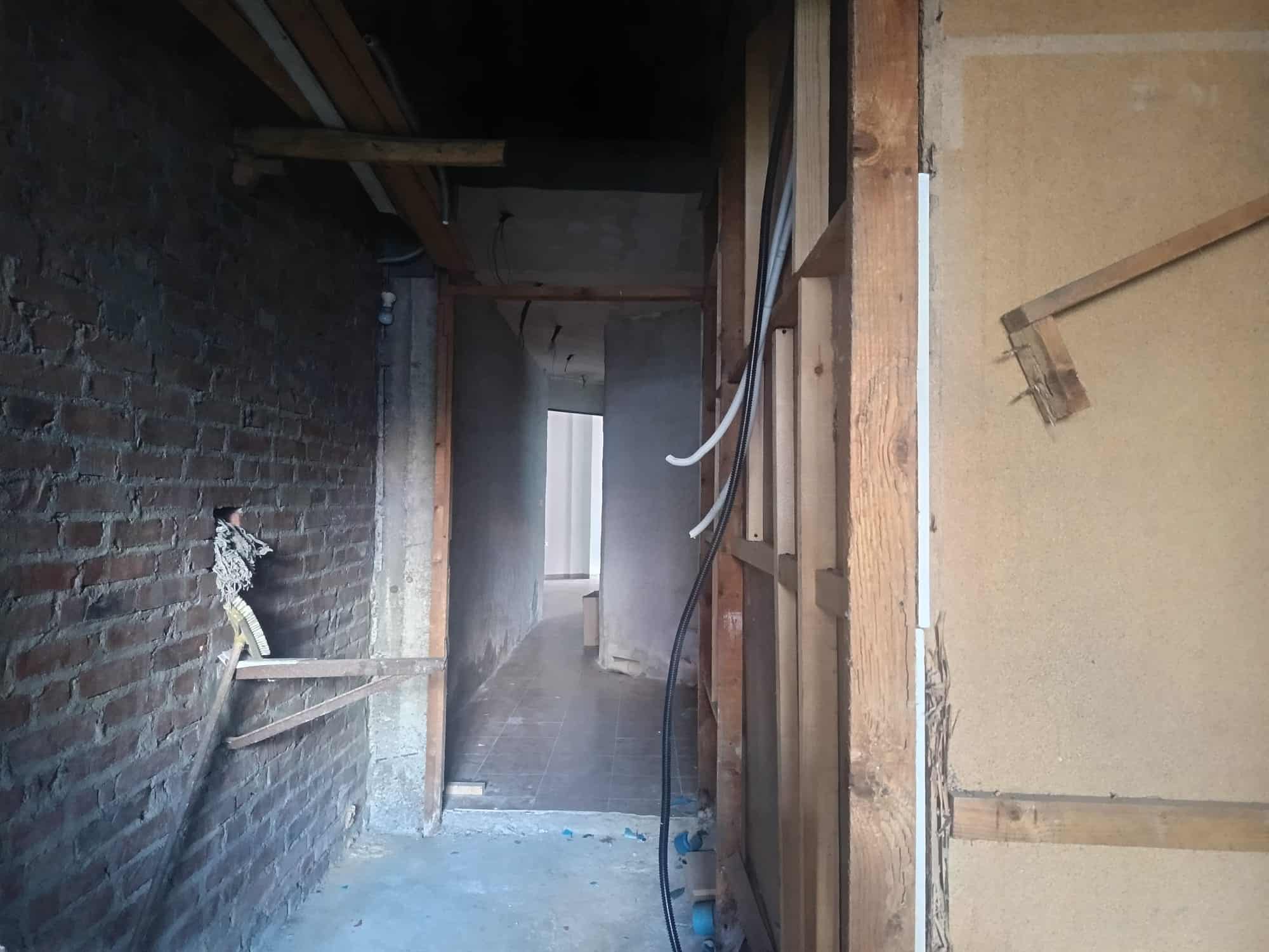 Prospettiva di un interno in fase di ristrutturazione edilizia, con pareti in mattoni e strutture in legno, pronto per lavori di rinnovamento e miglioramento degli spazi abitativi.