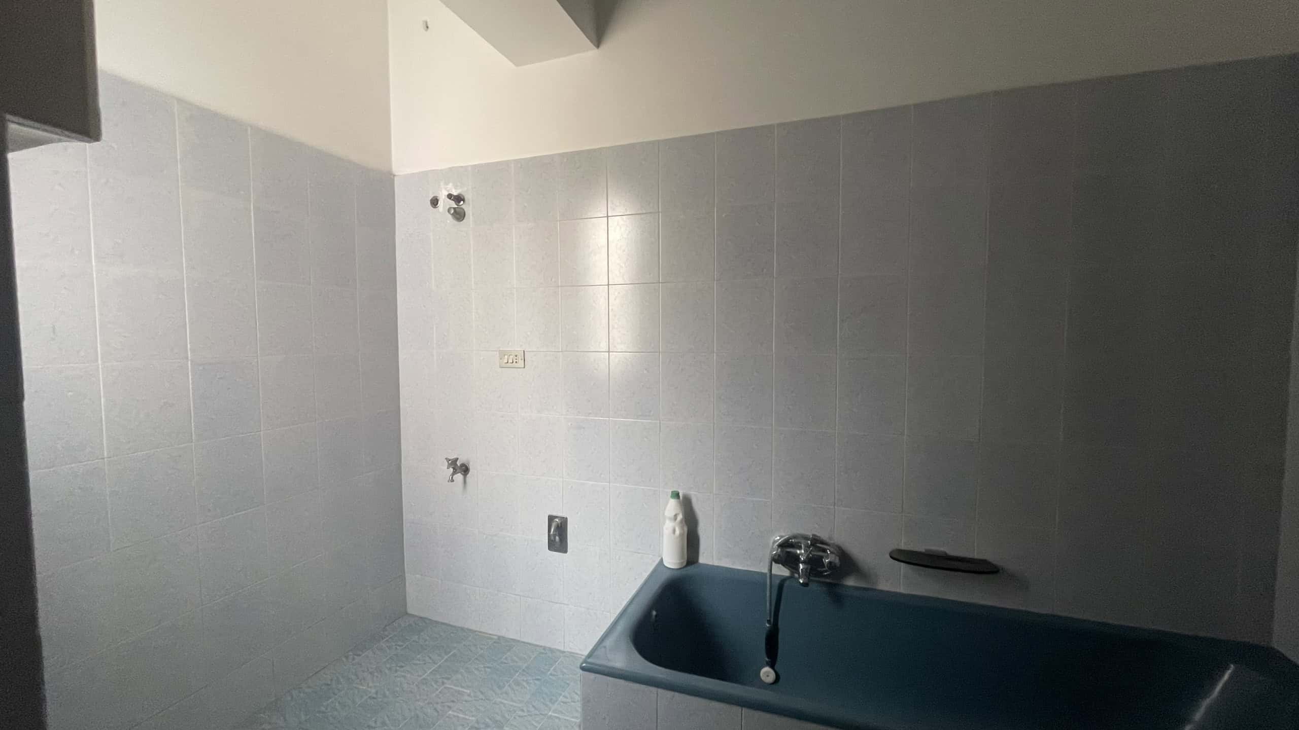 Lavanderia moderna con pareti rivestite in piastrelle grigie e vasca da bagno blu, ideale per spazi di servizio funzionali e eleganti.