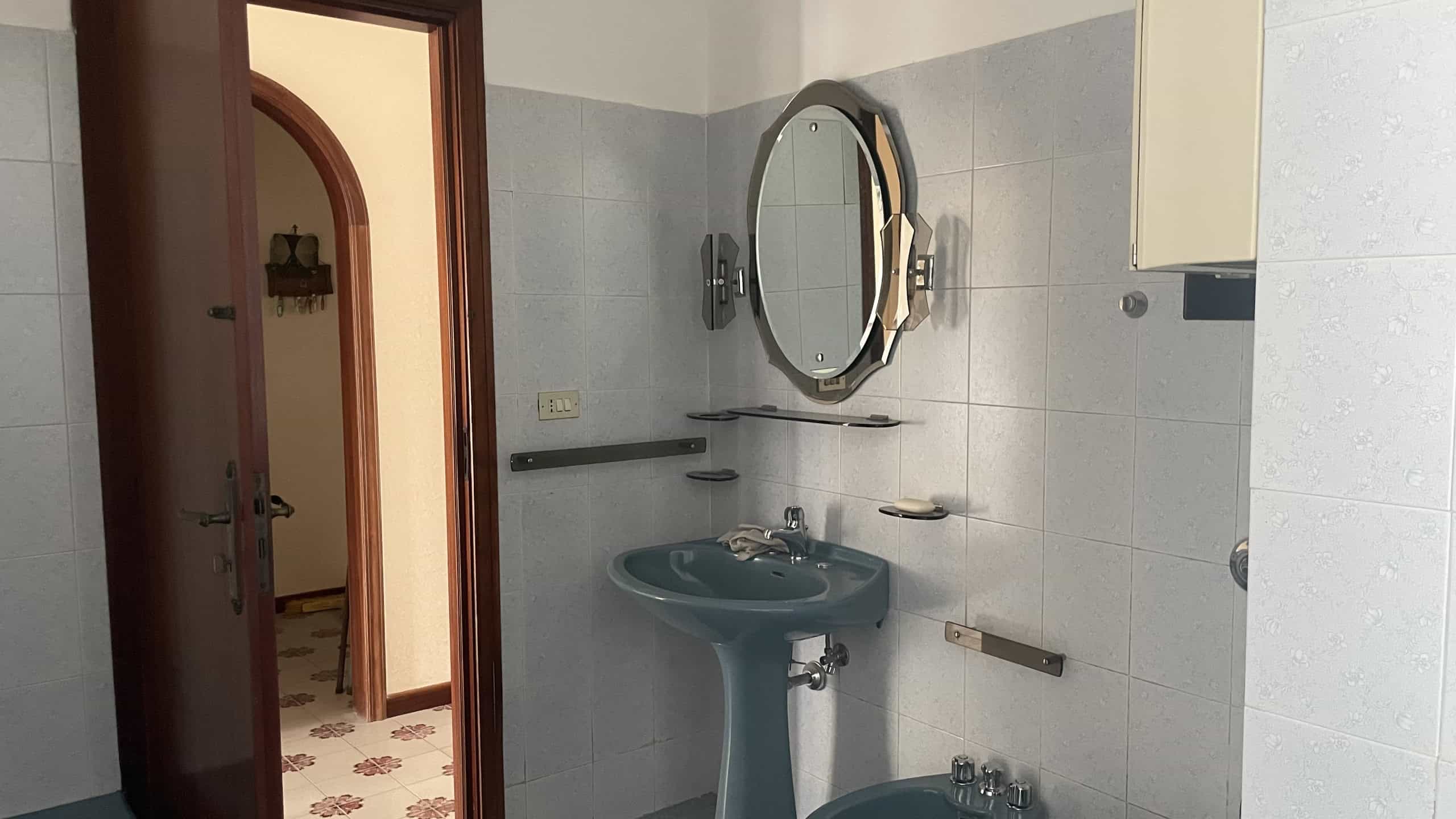 Spazzolino da denti e accessori nel bagno di una casa moderna, con lavabo e specchio rotondo, ambiente pulito e ben organizzato, ideale per immagini di interni di proprietà residenziali di NextCasa.