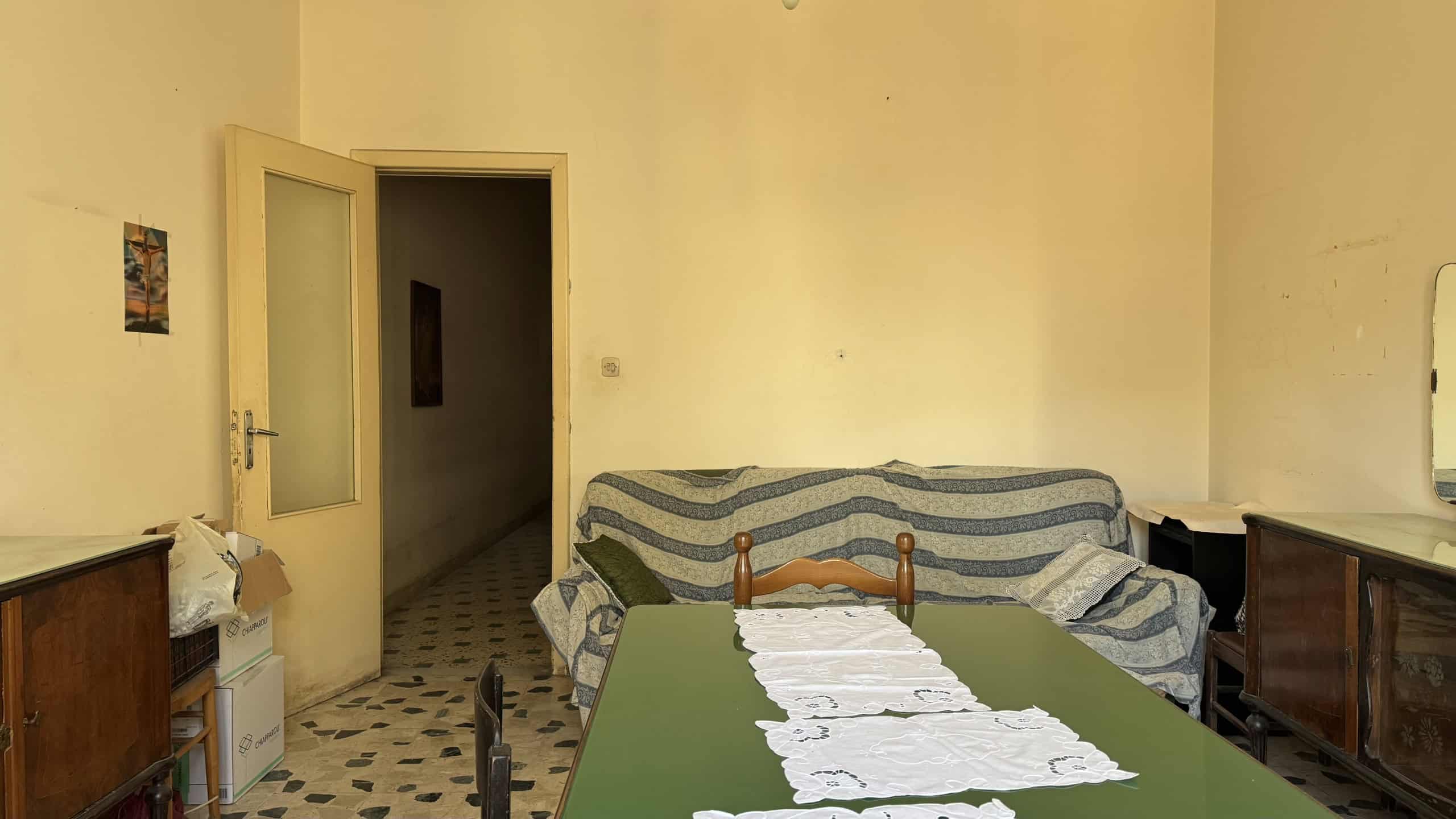Ampia sala da pranzo con tavolo verde, coperto da una tovaglia bianca, e divano con copertura a righe blu e beige, in un ambiente domestico luminoso e accogliente.