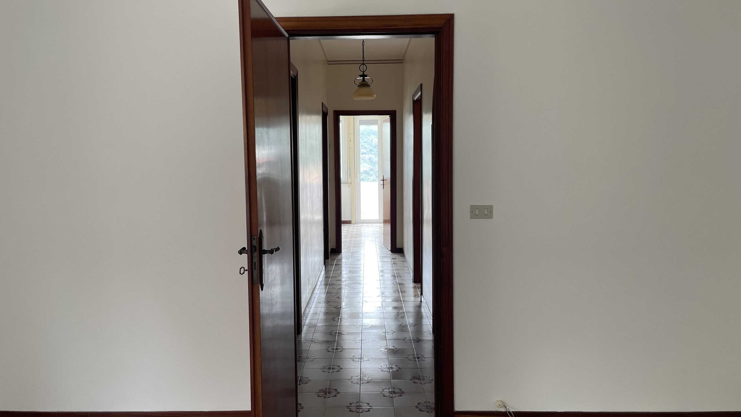 Ampio corridoio interno di un appartamento con pareti bianche e pavimento in piastrelle decorative, illuminato da luce naturale proveniente da una finestra sullo sfondo.