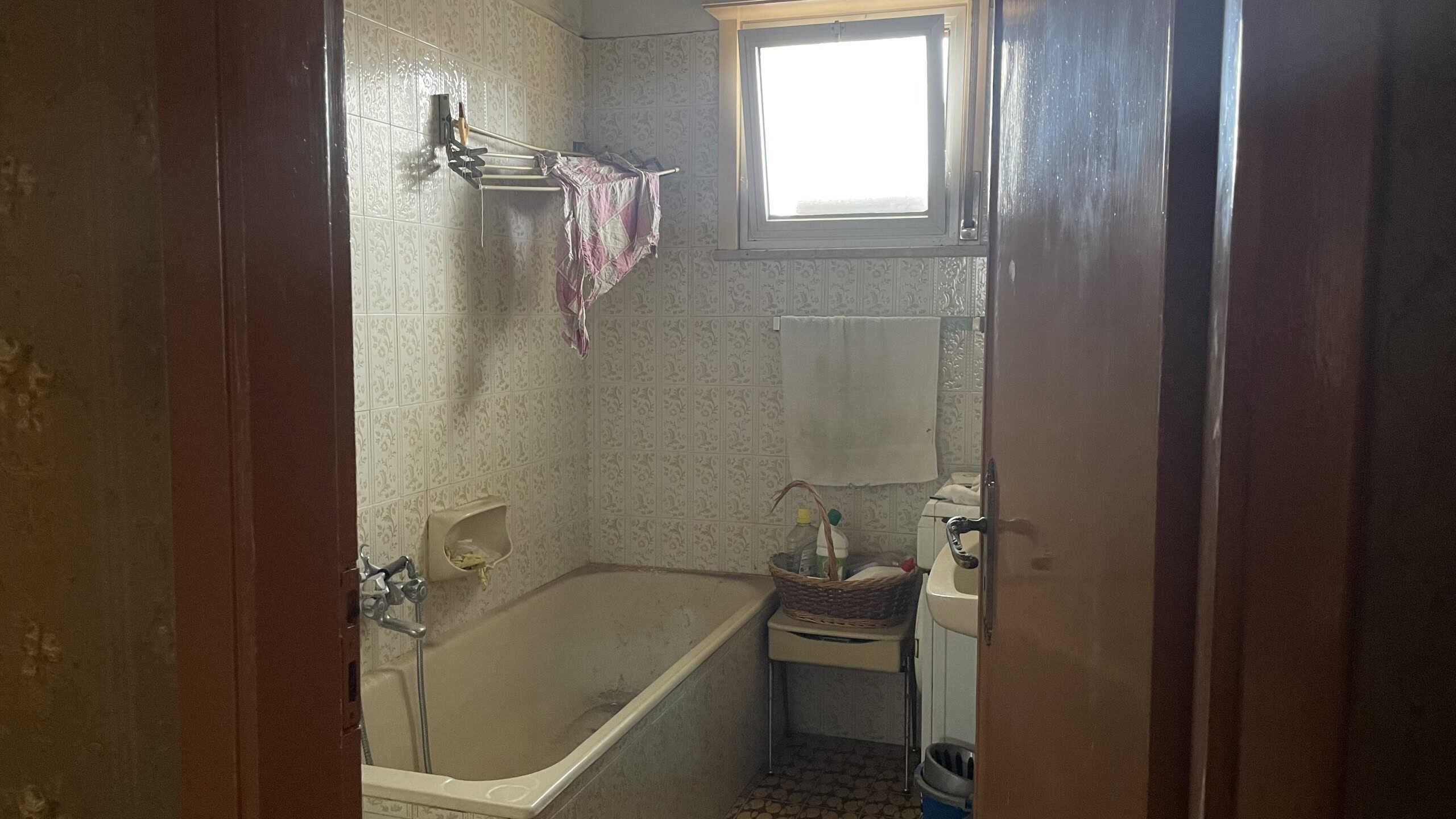 Acqua calda e lavatrice in un bagno di casa, con pareti rivestite in piastrelle beige e finestra naturale.