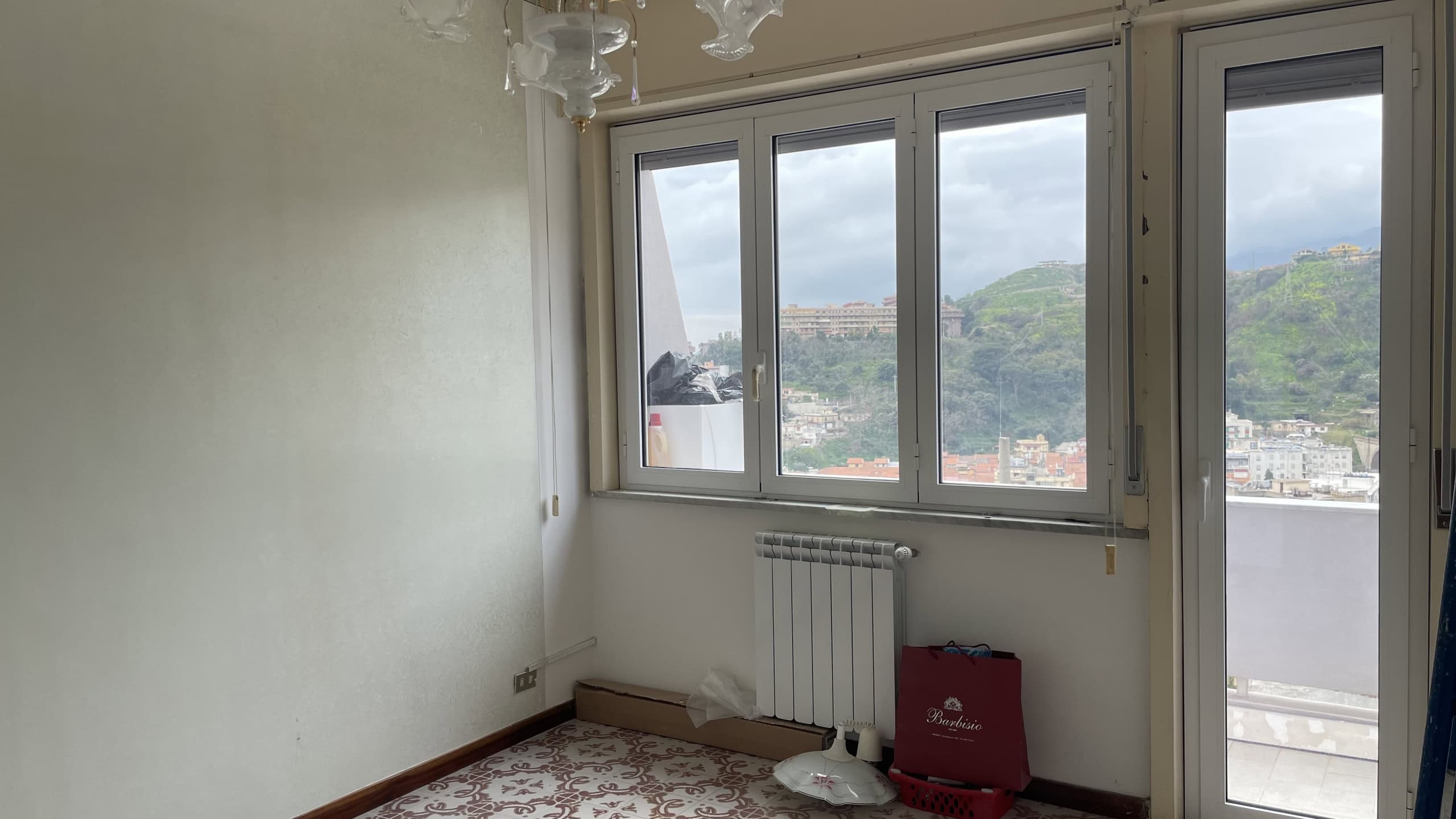 Ampio balcone con vista panoramica su colline e città, luminoso e arioso, ideale per relax e momenti di convivialità, con finestre grandi e accesso al terrazzo.
