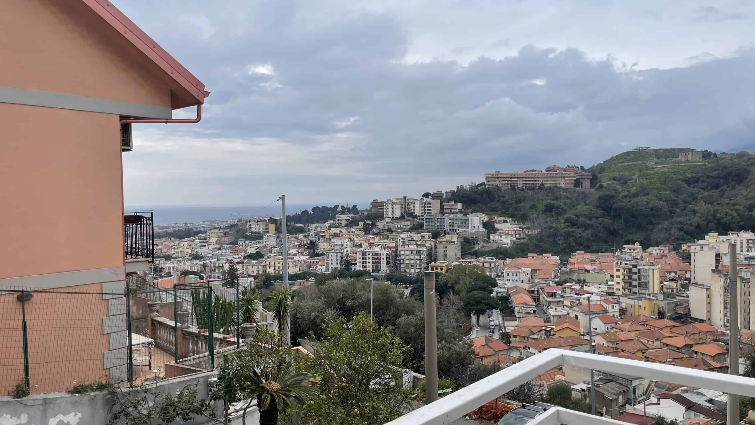 Vista panoramica della città di Napoli con il Vesuvio sullo sfondo, vista da un balcone di un appartamento residenziale, con case e edifici che si estendono fino al mare.