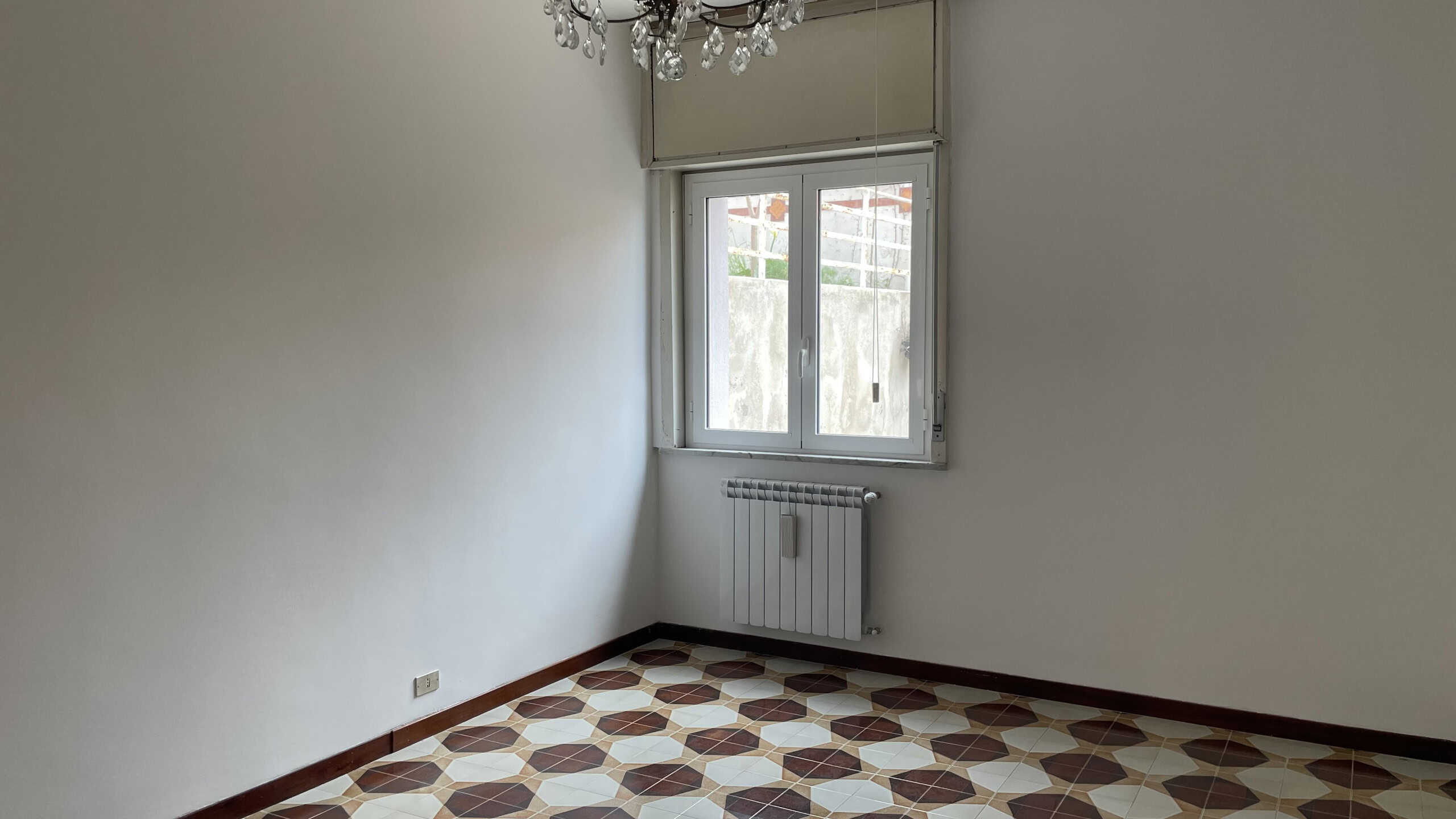 Appartamento vuoto con pareti bianche, finestra e pavimento in piastrelle geometriche, pronto per essere arredato e personalizzato. Ideale per chi cerca una soluzione abitativa luminosa e spaziosa.