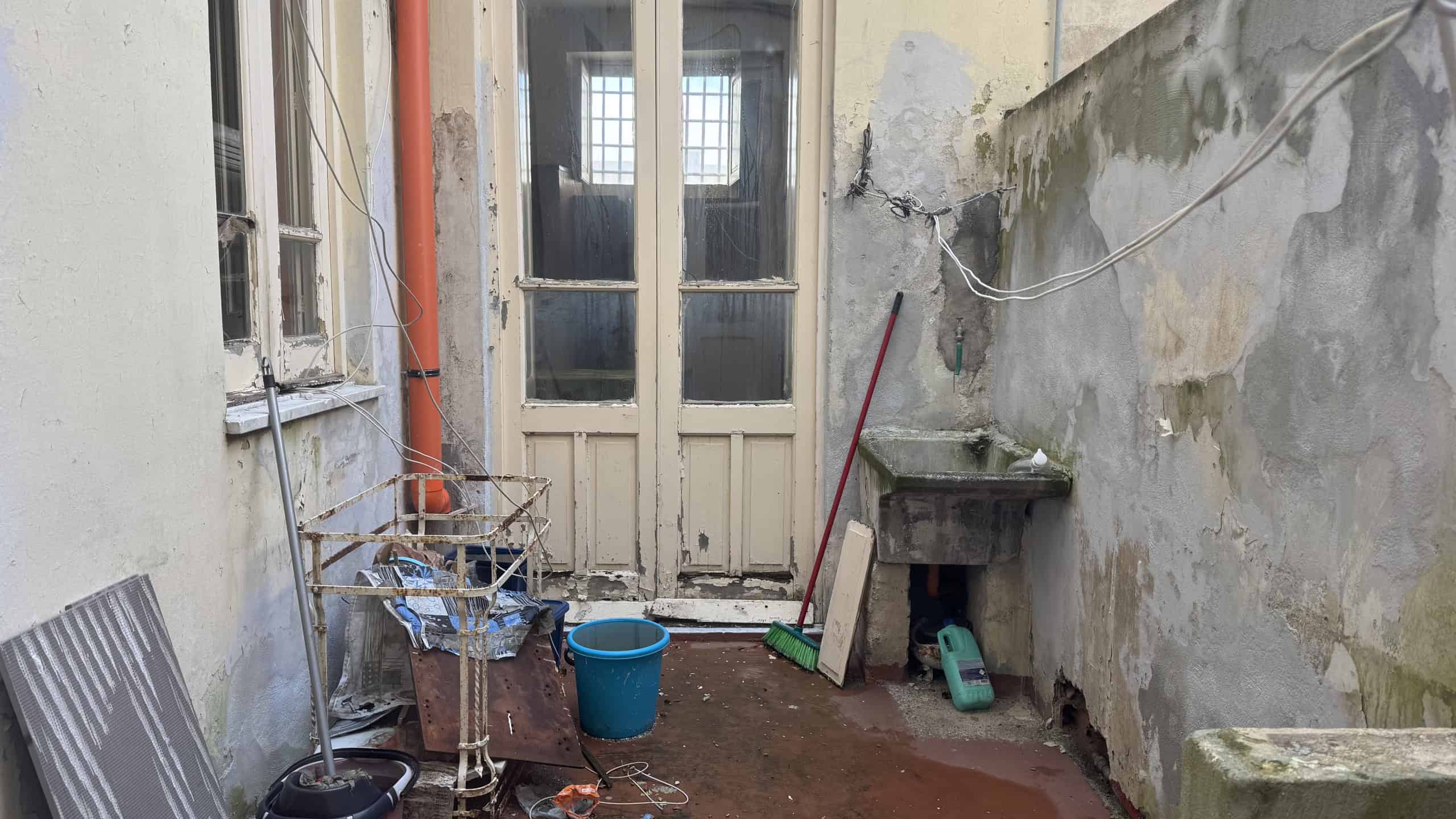 Piatto di servizio esterno con lavandino e attrezzi, area di lavoro in cortile con pareti in pietra e accesso a una porta finestra. Ideale per ristrutturazioni e miglioramenti di immobili residenziali.