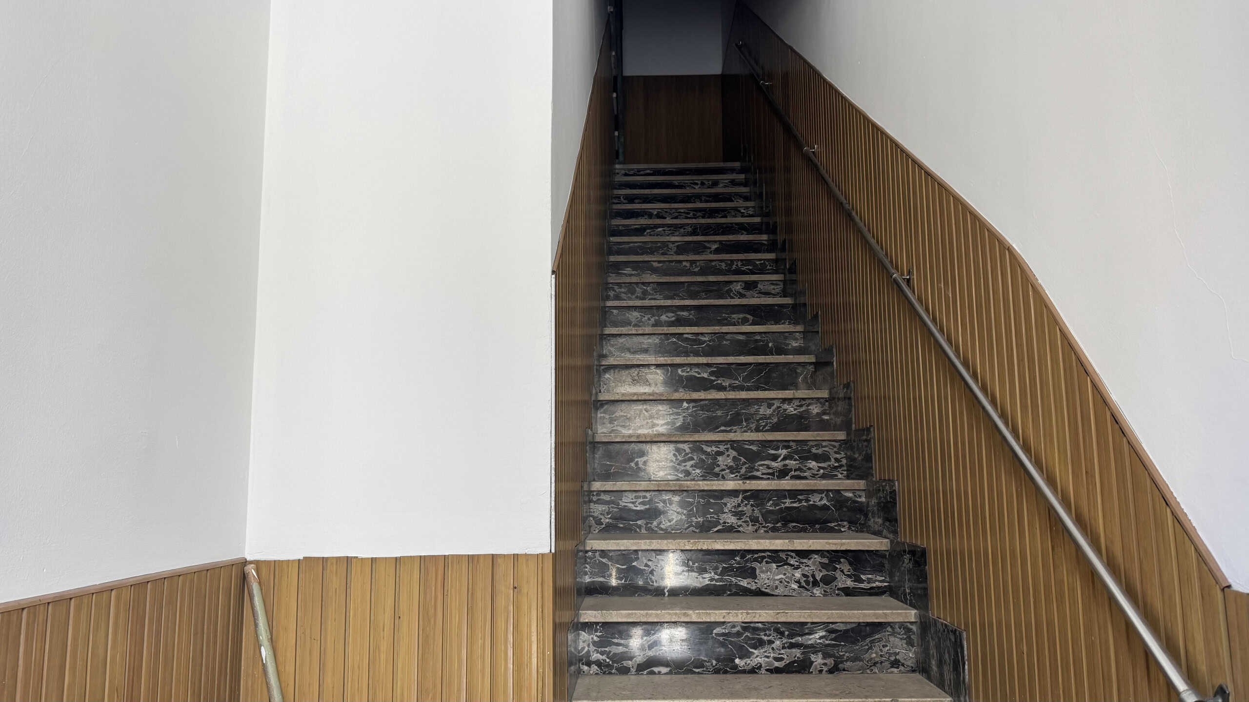 Scale da interno con ringhiera in legno e gradini in marmo nero, parte di un moderno progetto di ristrutturazione edilizia. Design elegante e funzionale per ambienti residenziali di alta qualità.