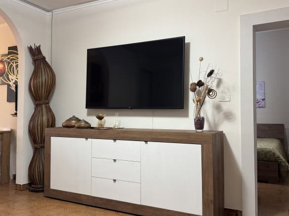Elegante soggiorno con TV a schermo piatto, mobile TV in stile moderno, decorazioni floreali e arredi minimalisti, ideale per ambienti di casa accoglienti e di design.