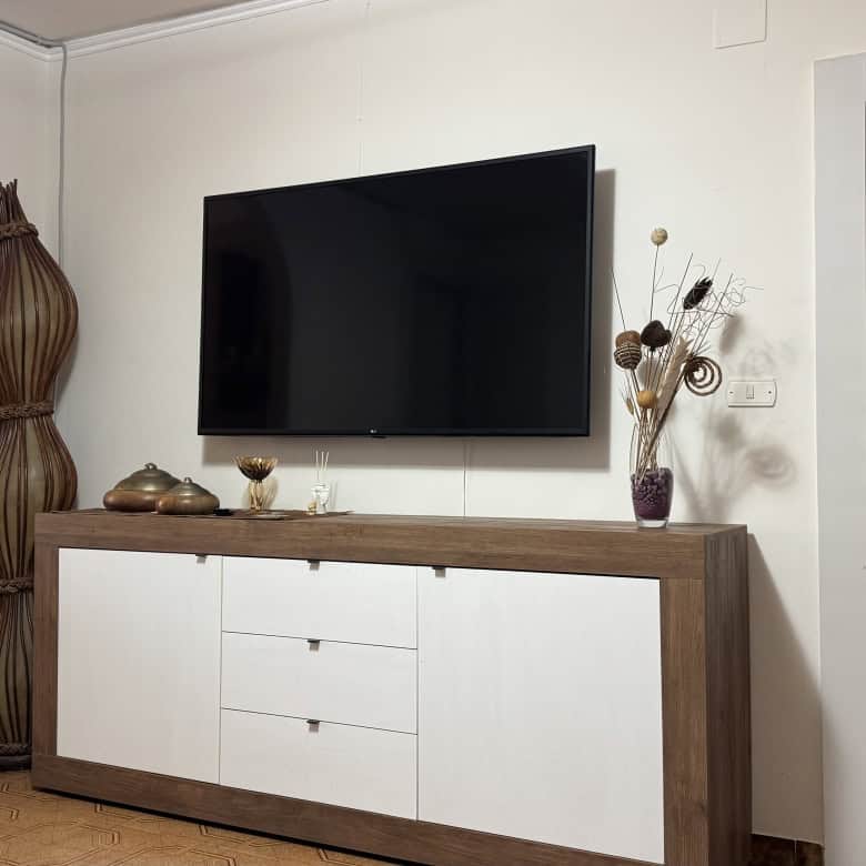 Elegante soggiorno con TV a schermo piatto, mobile TV in stile moderno, decorazioni floreali e arredi minimalisti, ideale per ambienti di casa accoglienti e di design.